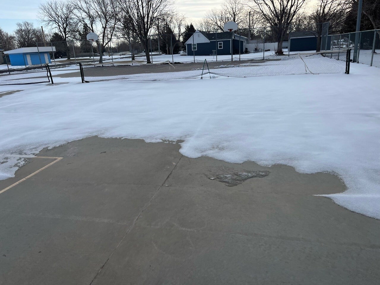 Snow-covered outdoor tennis courts showing winter conditions that prevent court resurfacing