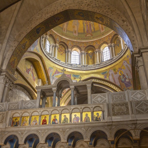 Interior of a cathedral featuring arched ceilings, ornate frescoes, and painted religious figures, with a dome and arched windows above.