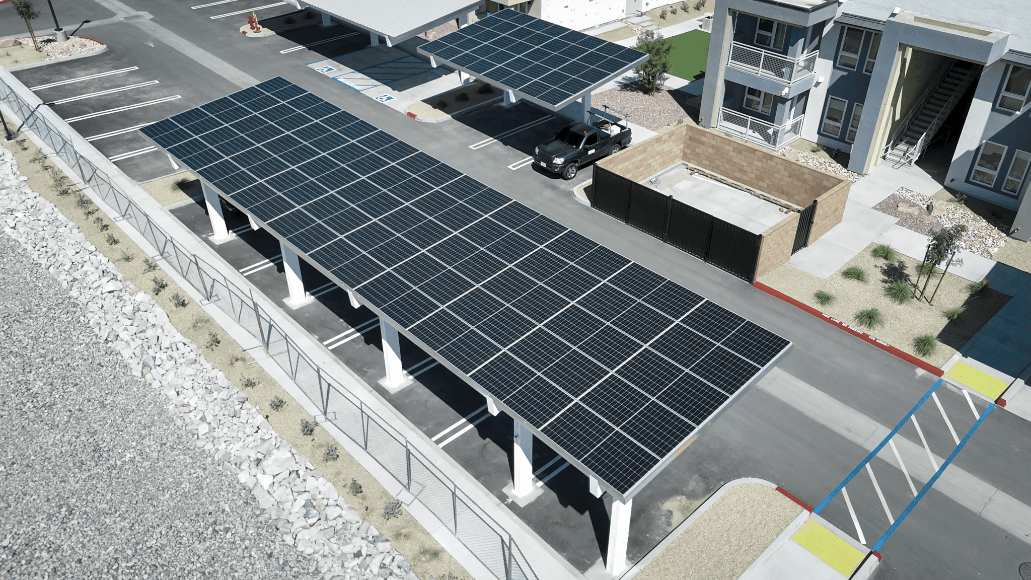 Aerial view of a long solar carport canopy shading a row of parking spaces beside a commercial building