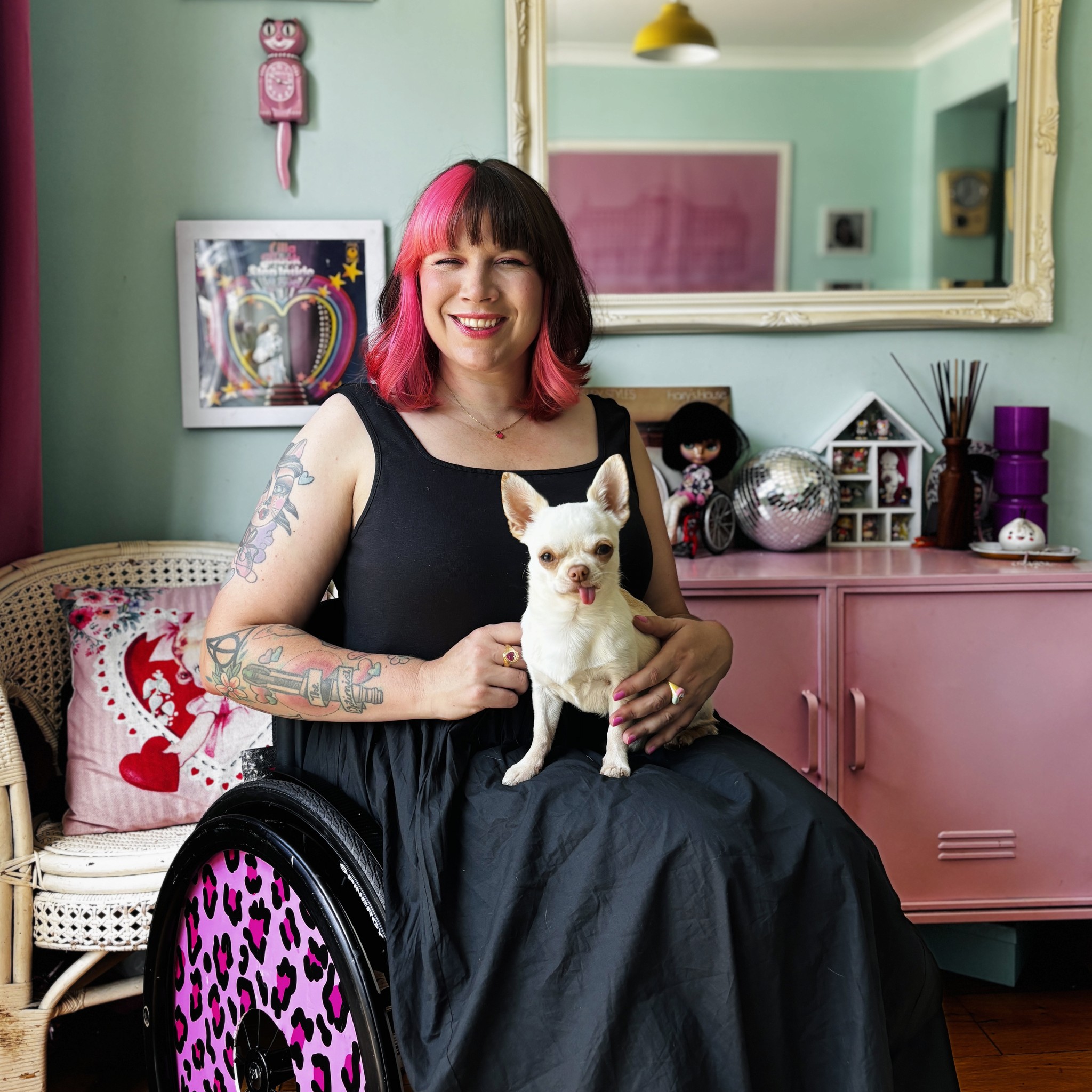 Nina is sitting in her wheelchair with pink leapord print wheel cover, holding her chihuahua with a big smile on her face.