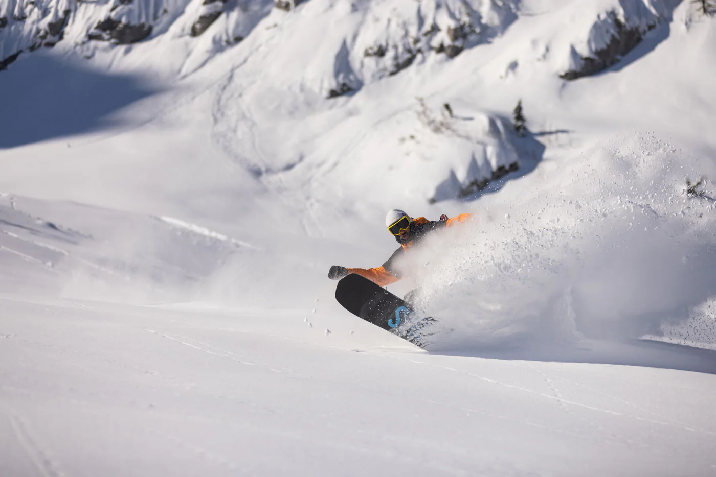 Een freeride snowboarder die een diepe een energieke powderspray maakt.