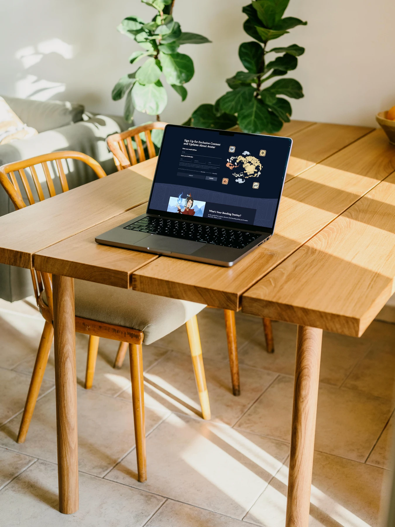 Fluid web design of a newsletter sign-up form and illustrated character card shown on a laptop in a sunlit room with wooden table and plants.