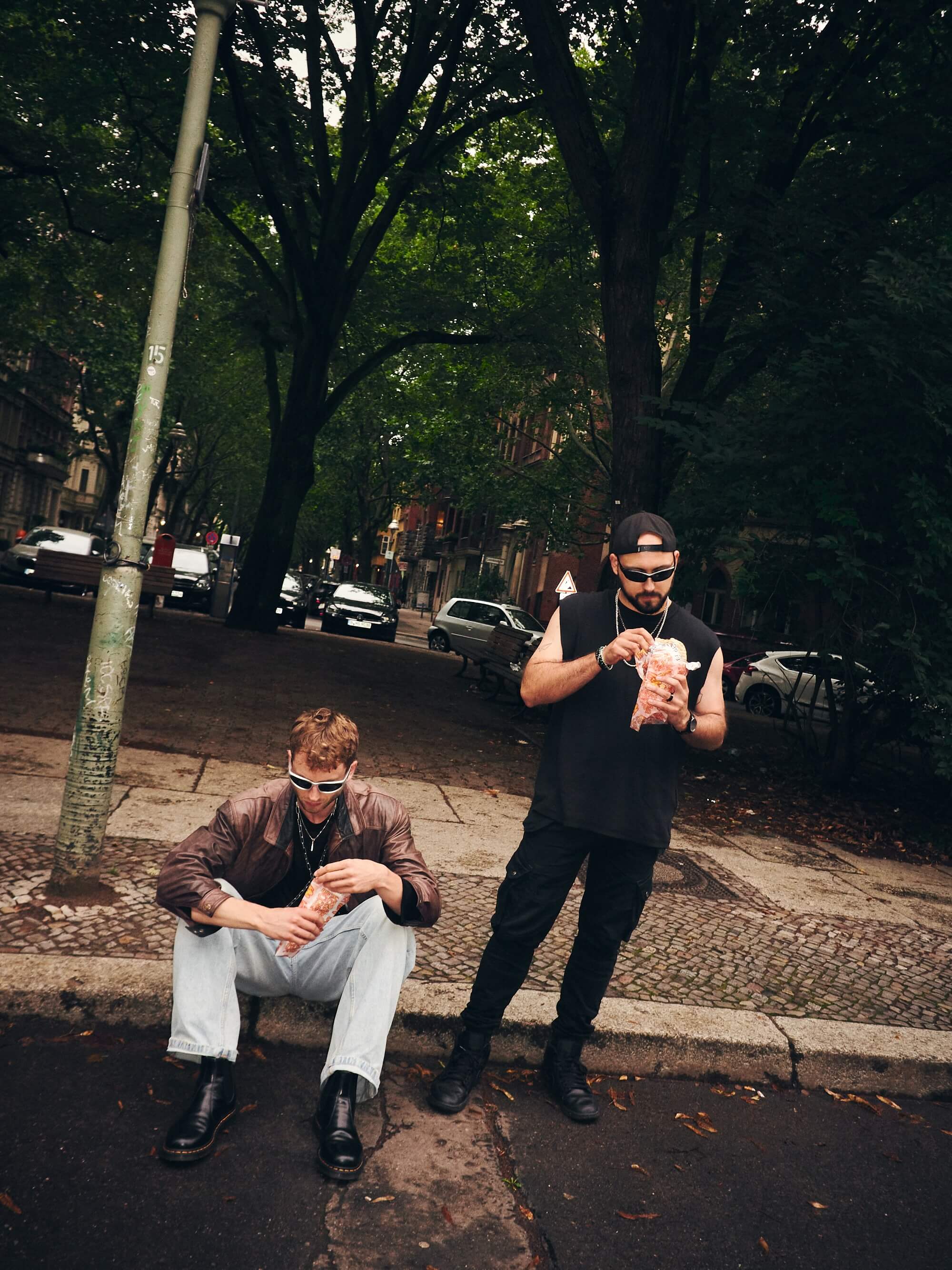 Two people in techno-inspired outfits sitting outdoors eating kebabs