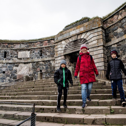 Three people in warm clothing walking down stone steps in front of an old stone fortification.