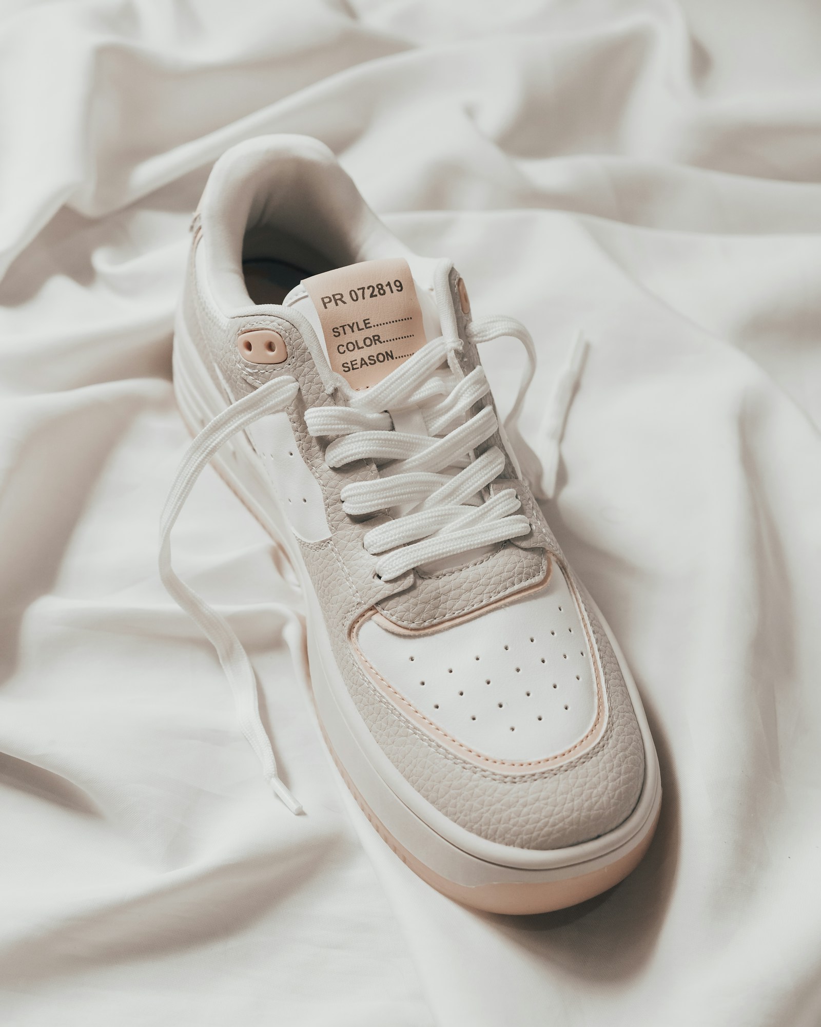 Cream sneaker with loose laces laid on white fabric