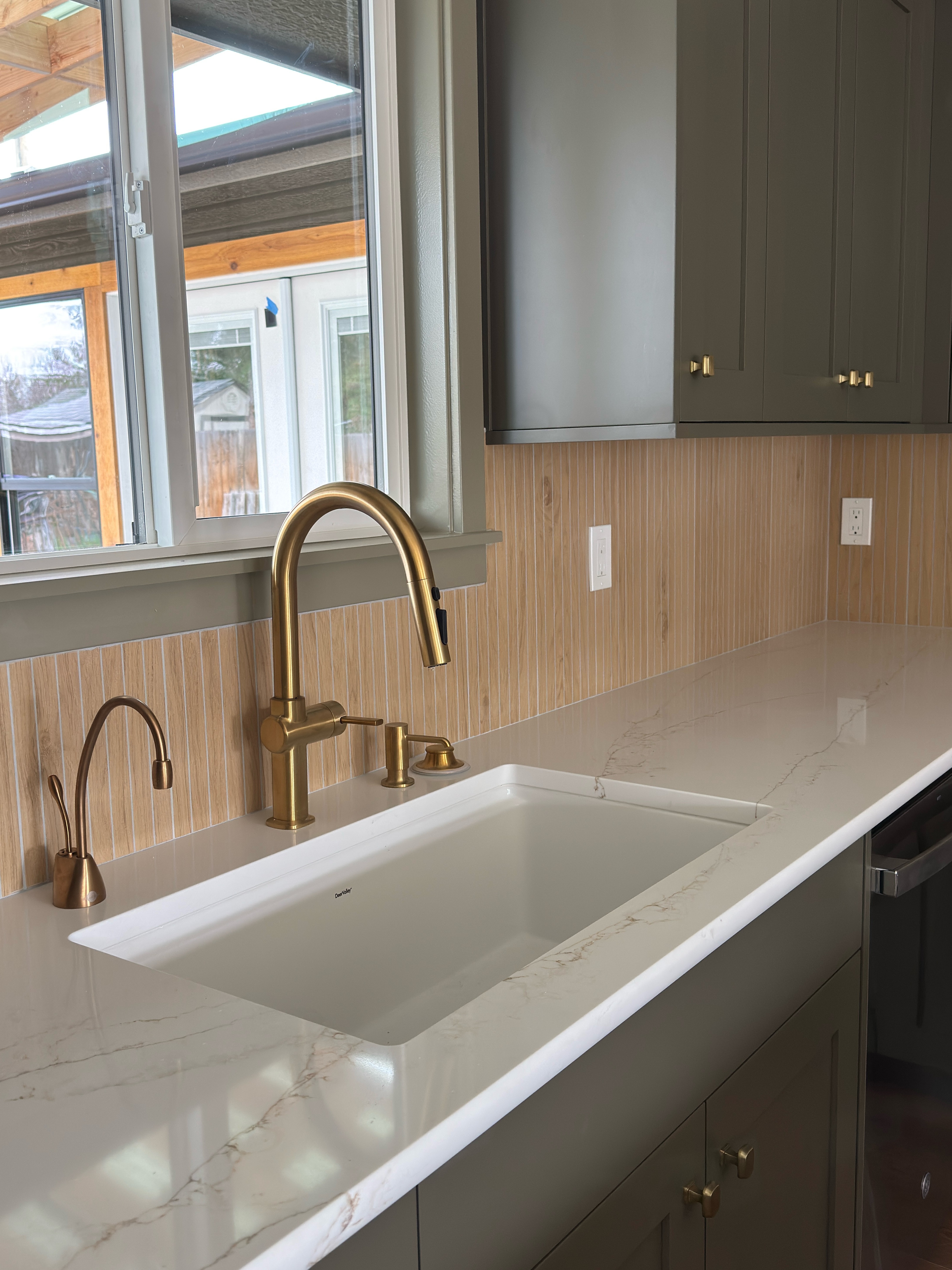 Smiling young woman with long hair standing against a dark green background, holding a finger to her chin.