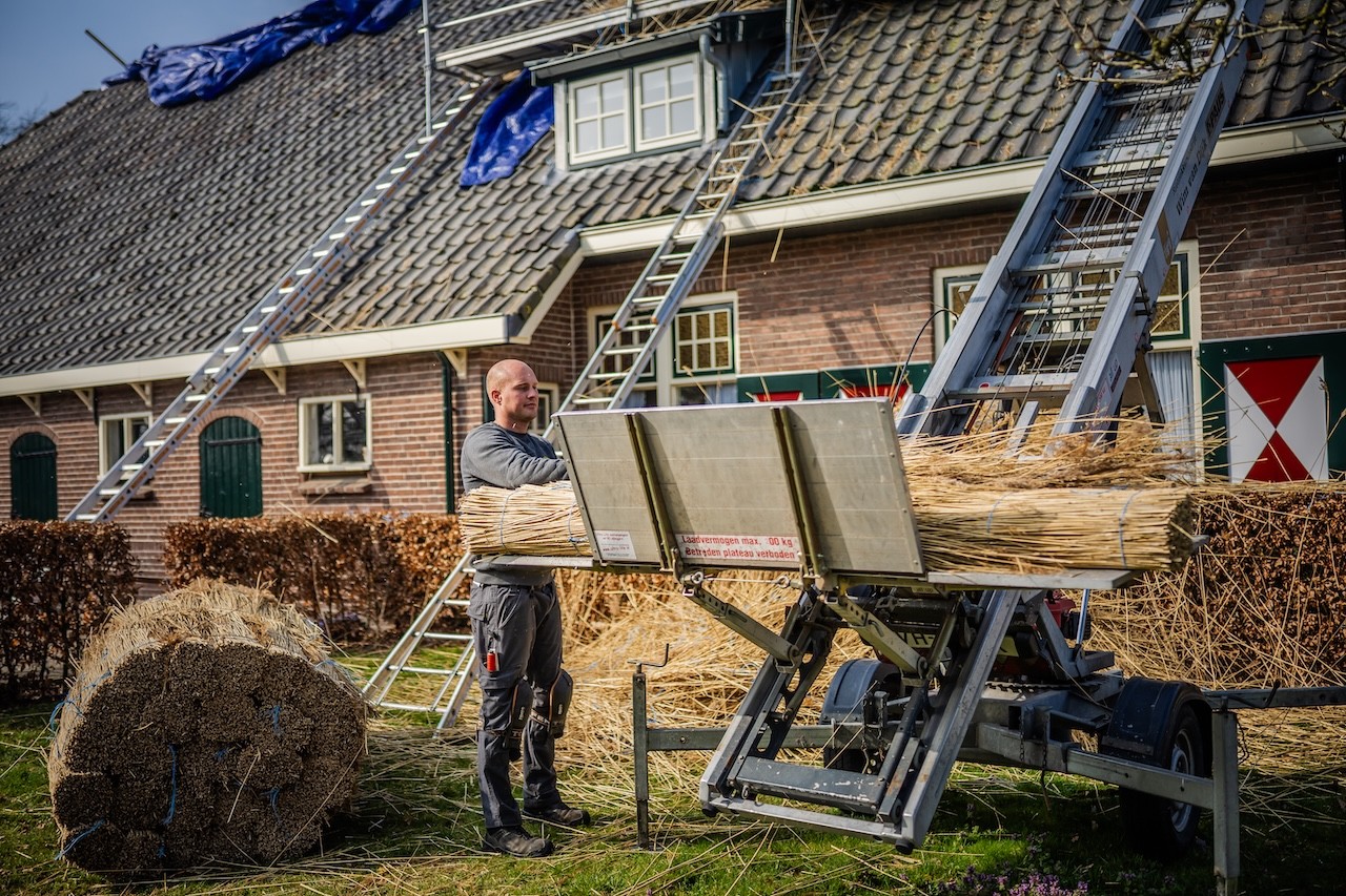 Rietdekker van Rietdekkersbedrijf van Dijk werkend aan de vervanging van dakpannen met een rieten dak