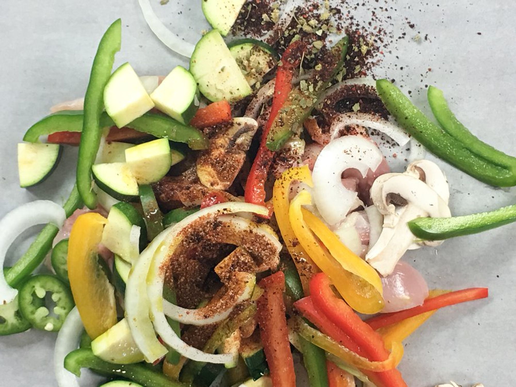 seasoned chicken and veggies being tossed on a baking sheet