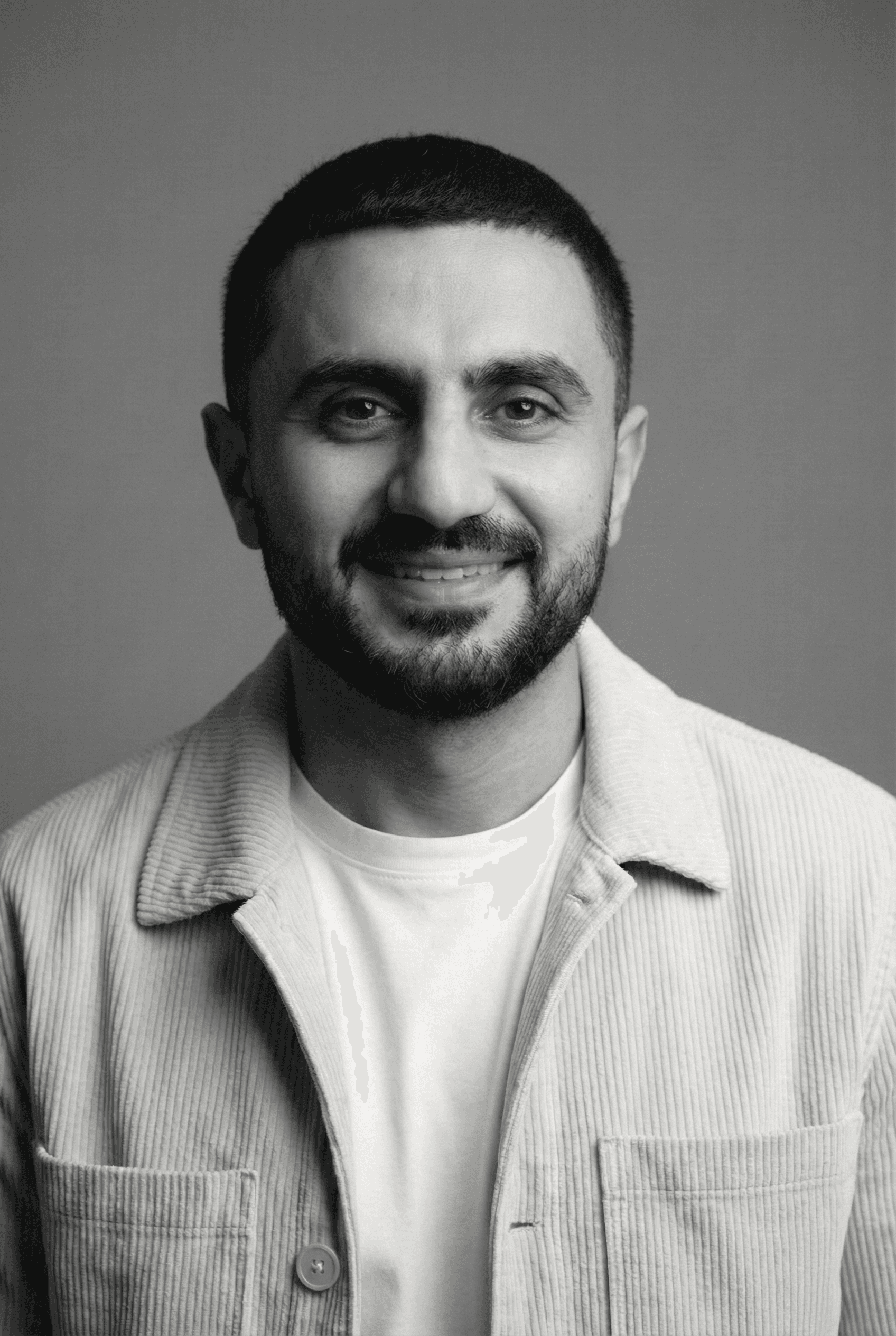 Portrait of a young man with short hair, wearing a dark t-shirt, against a plain background.