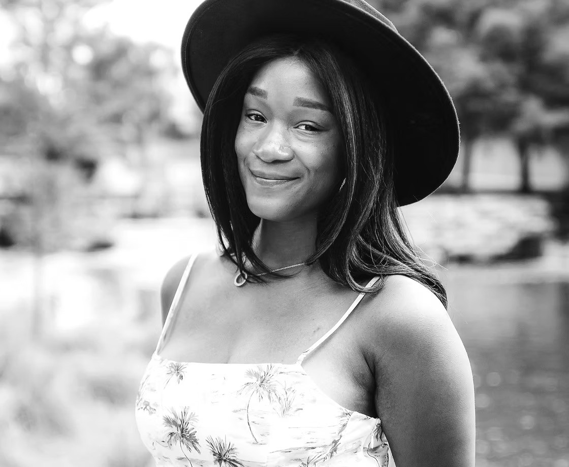 Black-and-white portrait of Tia Bailey, Artist and Founder, wearing a hat and smiling.