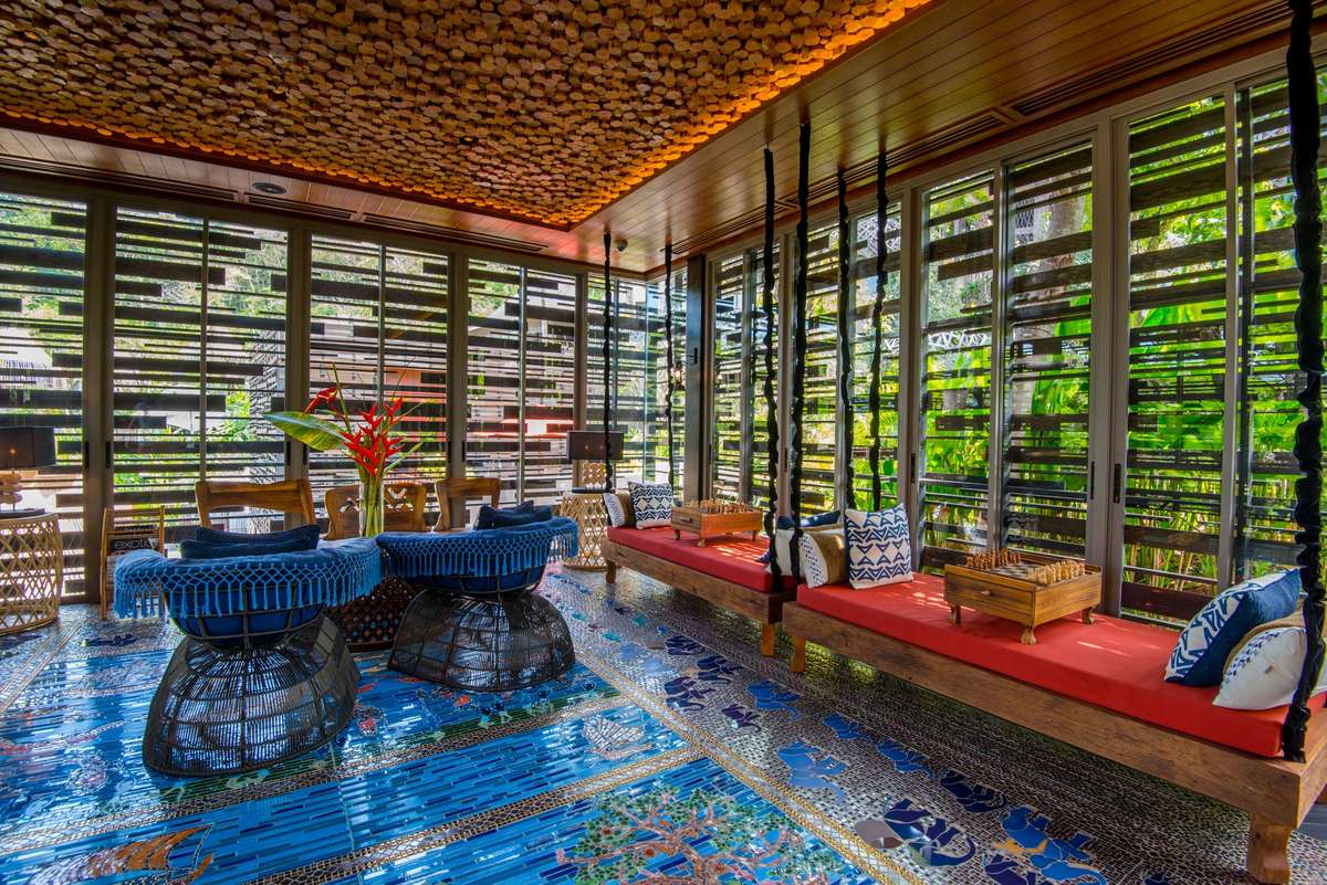 A vibrant lounge with blue mosaic tile floors, red cushioned seating, and a textured orange ceiling under warm lighting.