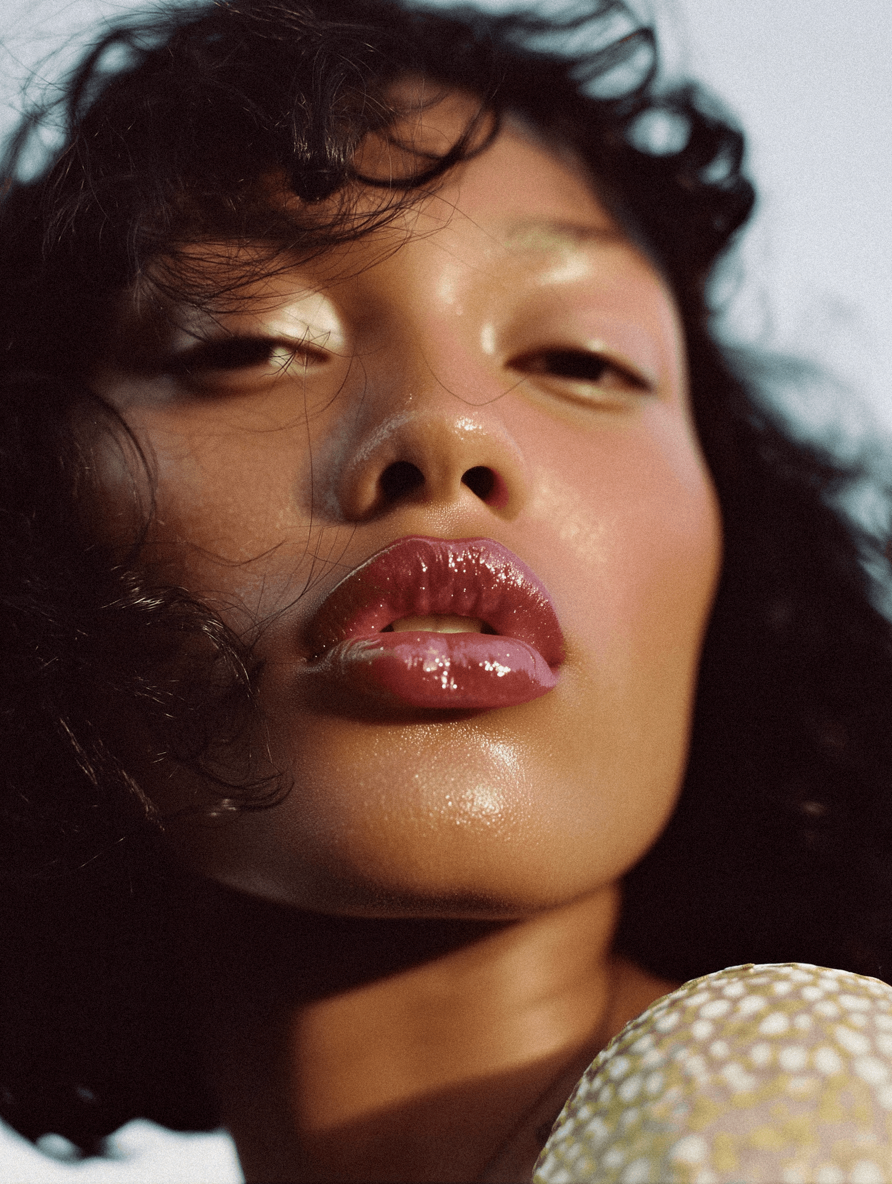Close-up portrait of a person with glossy lips, curly hair, and radiant skin, captured in soft lighting for an artistic effect.