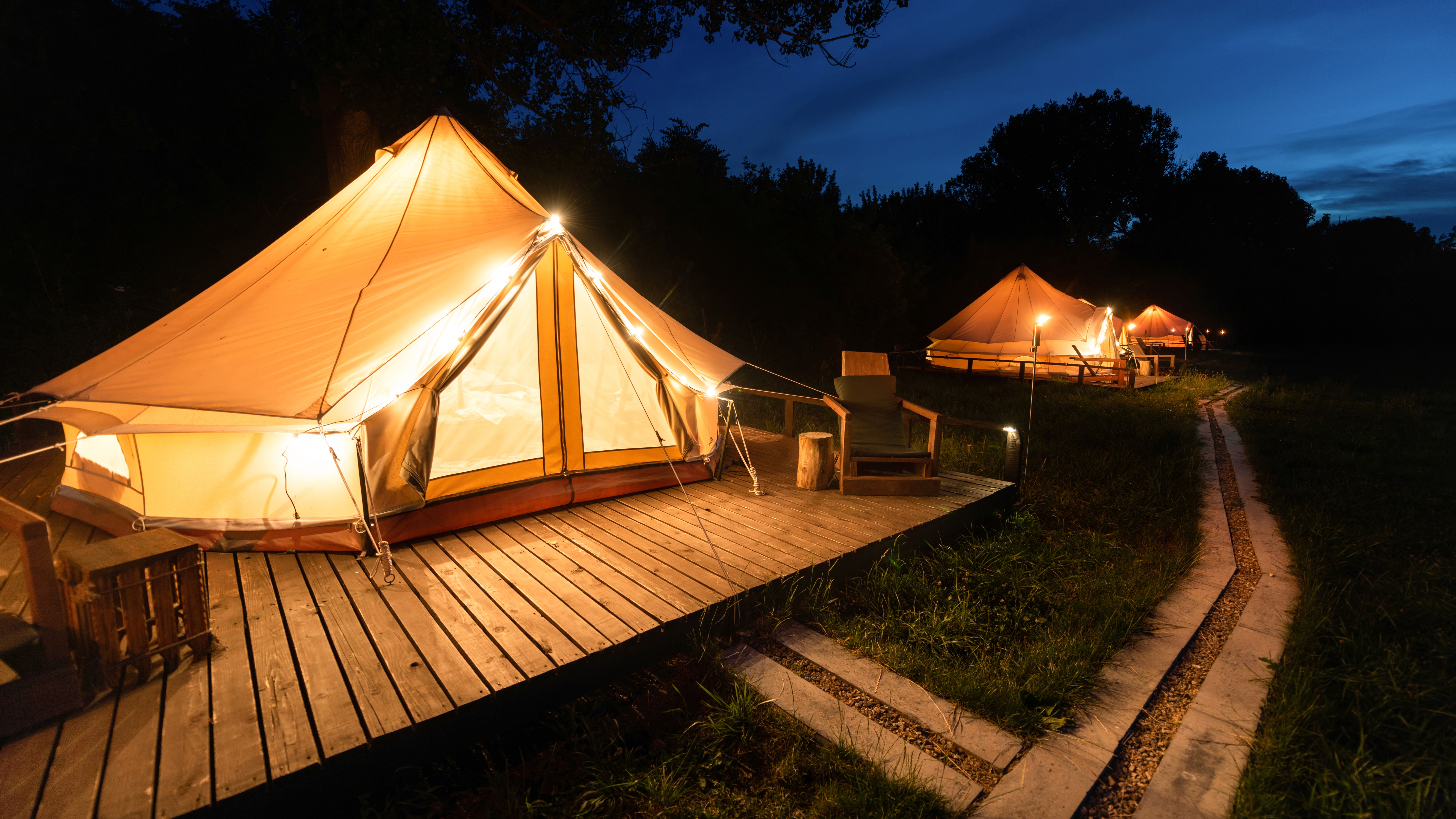 Tiendas de campaña tipo glamping iluminadas por la noche en un entorno natural rodeado de árboles.