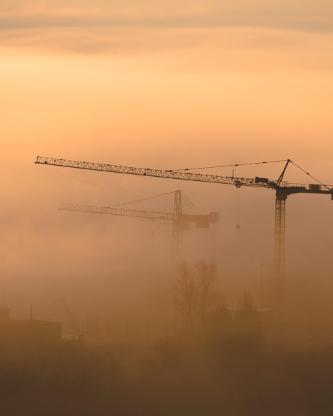 A crane suspended over a hazy, foggy orange-coloured city sky.