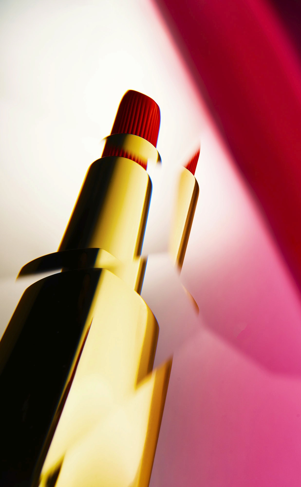 Close-up of a red lipstick against a colorful gradient background, highlighting its glossy texture and bold color.