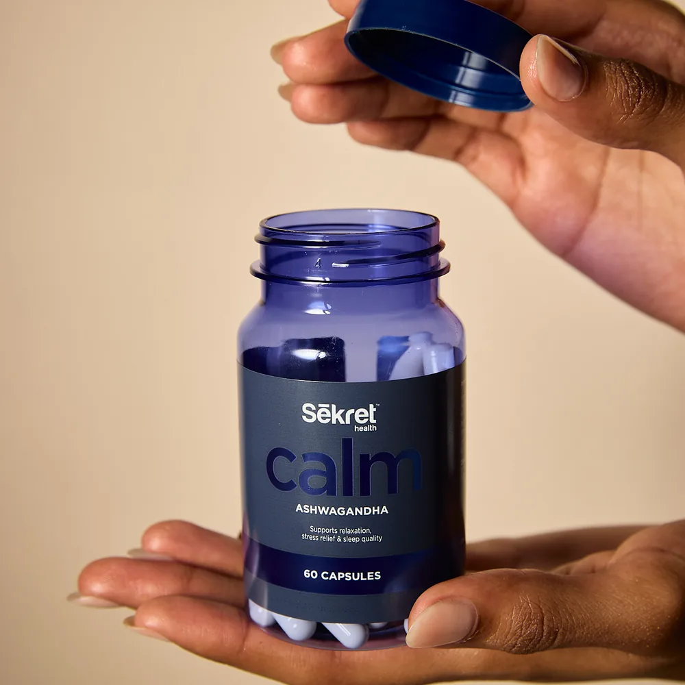 A hand opening a bottle of Sekret Calm ashwagandha capsules
