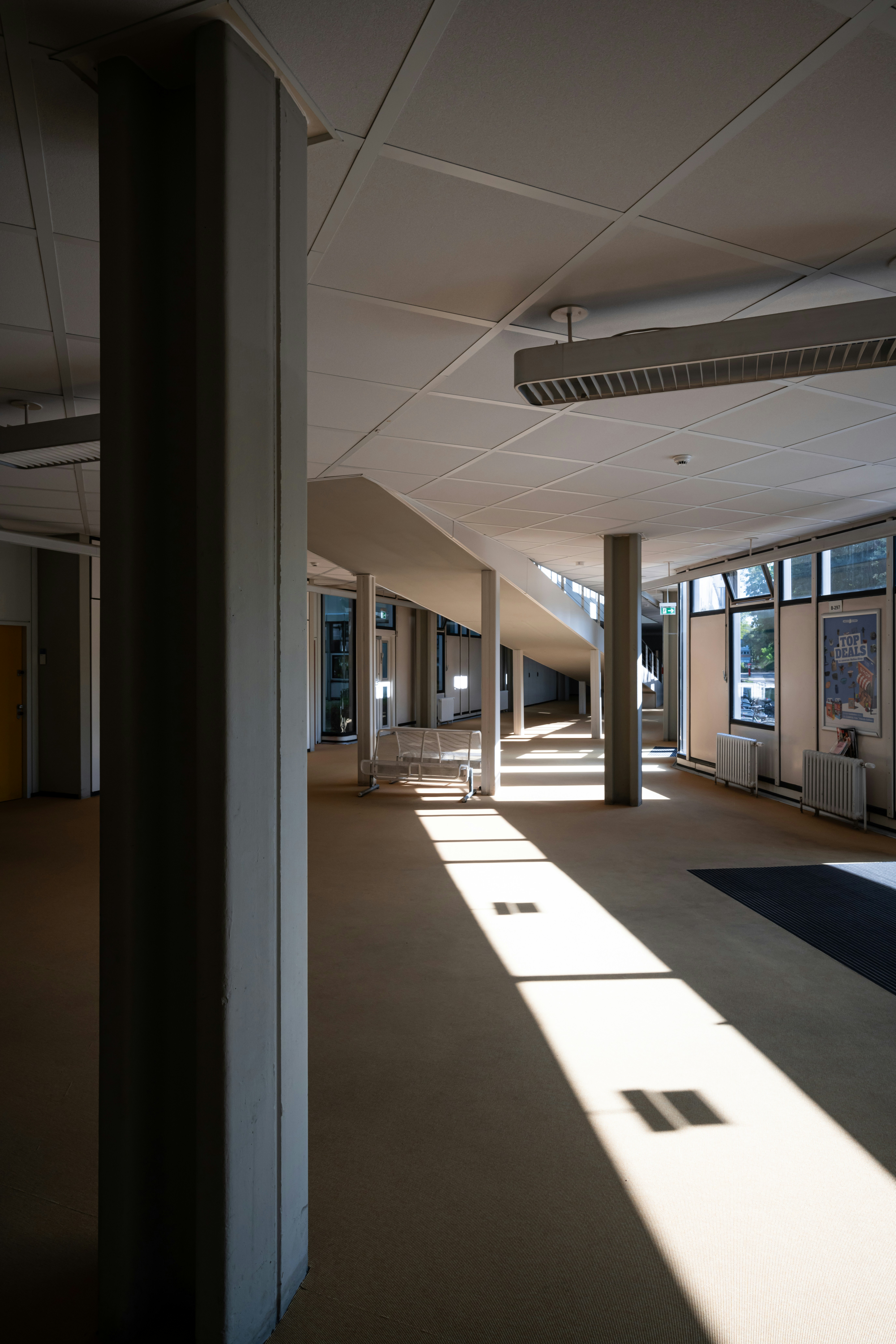 Interior view of a modern building, featuring a long light beam and columns casting shadows on the floor.