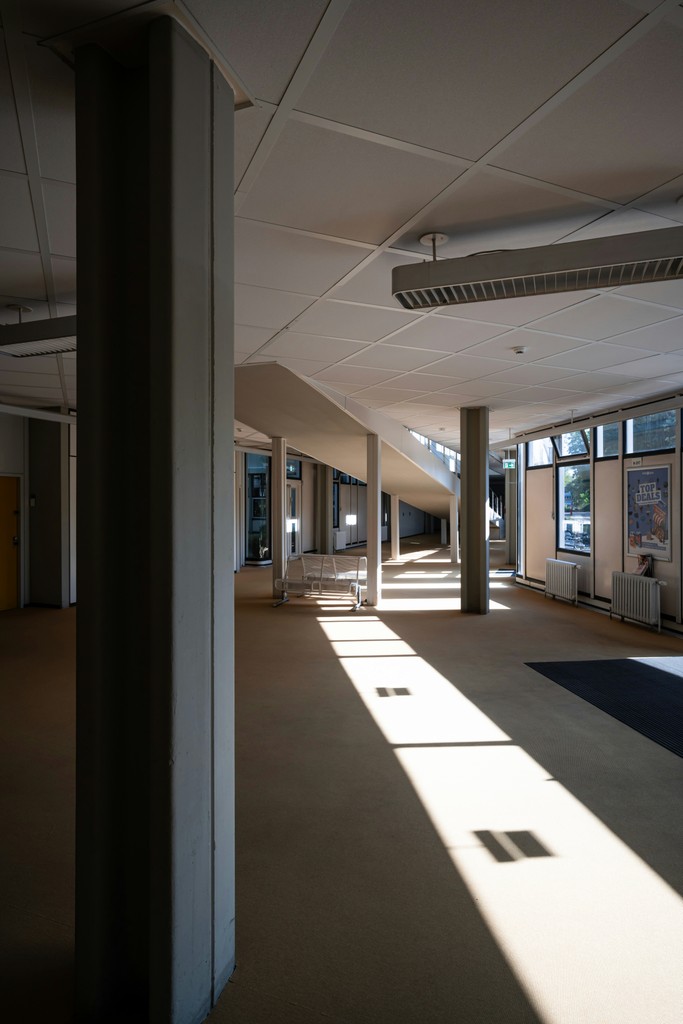 Interior view of a modern building, featuring a long light beam and columns casting shadows on the floor.