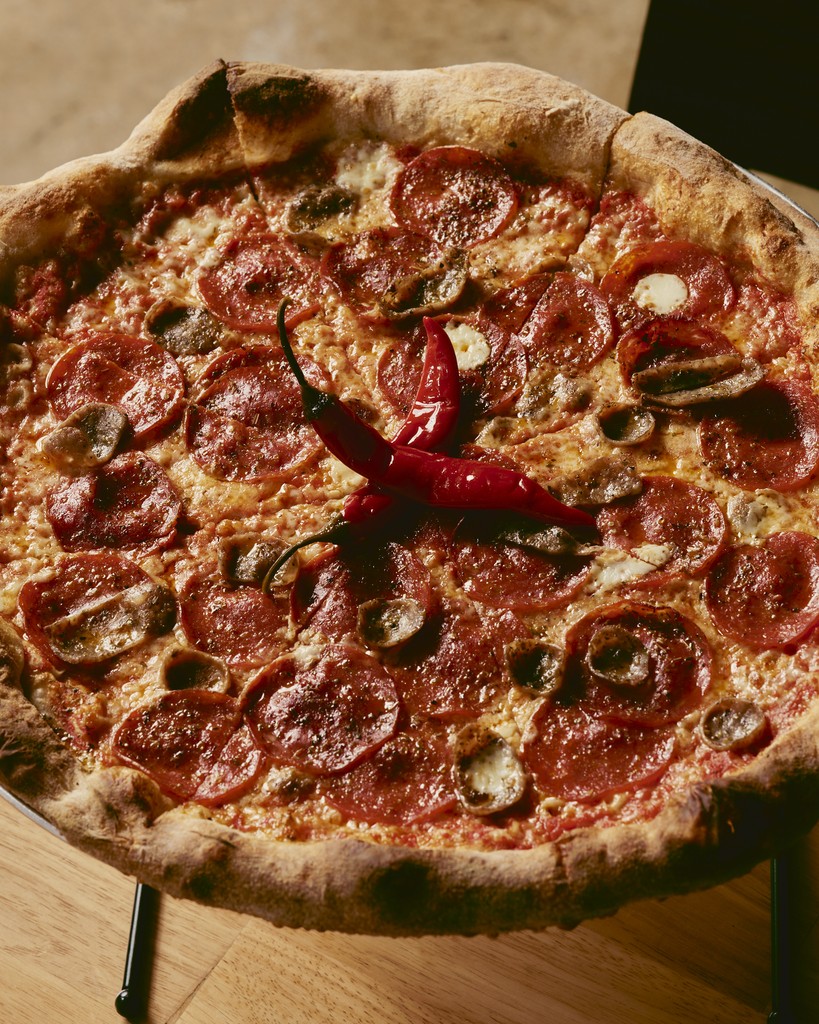 Close-up portrait of a person wearing a gray insulated hooded jacket with the hood up, showing their face framed by the hood against a light background.