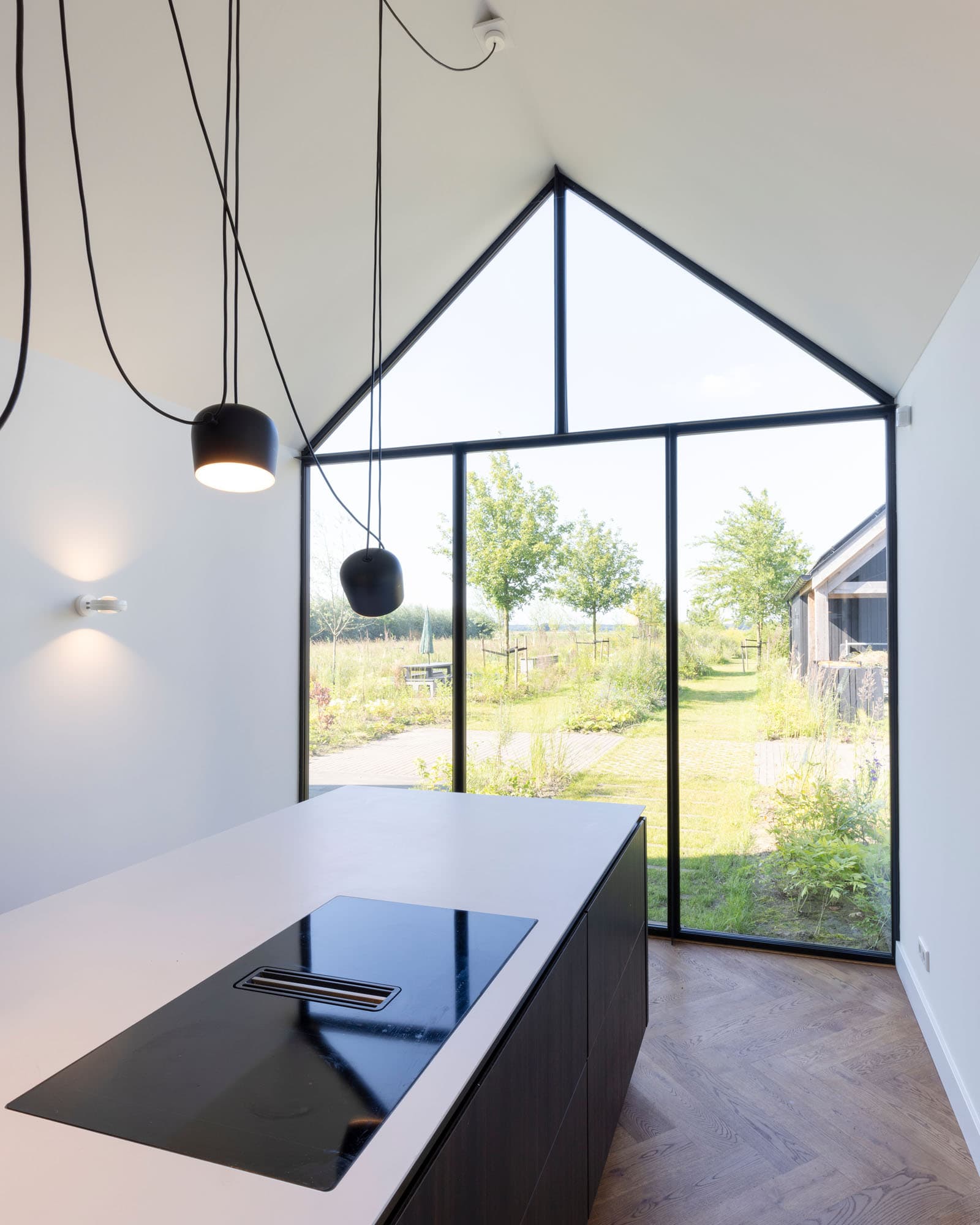 Detail van moderne keuken met houten kastenwand, wit kookeiland en stalen binnendeur
