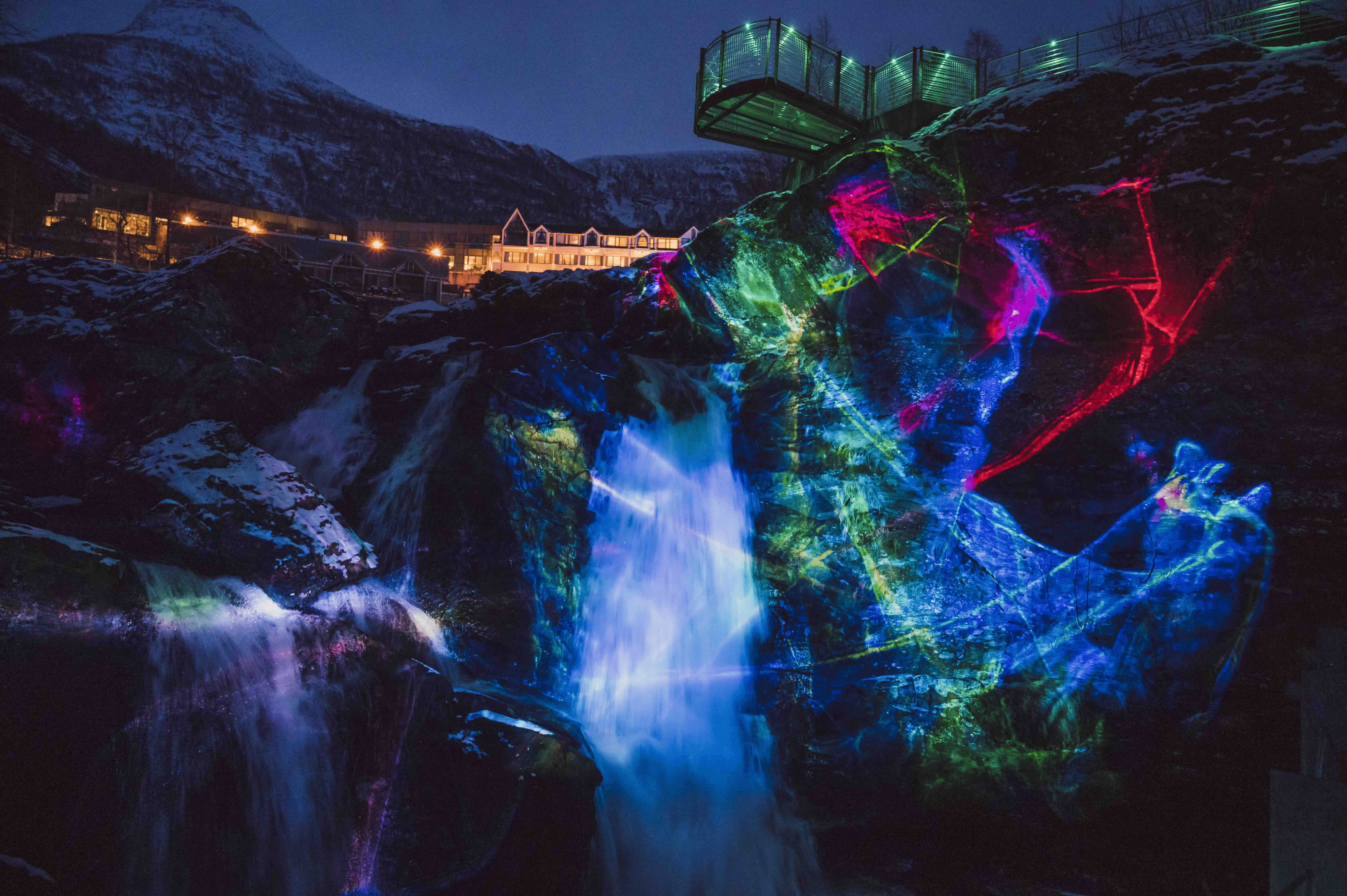 A vibrant, illuminated scene featuring colorful lights reflecting on water amidst dark surroundings.