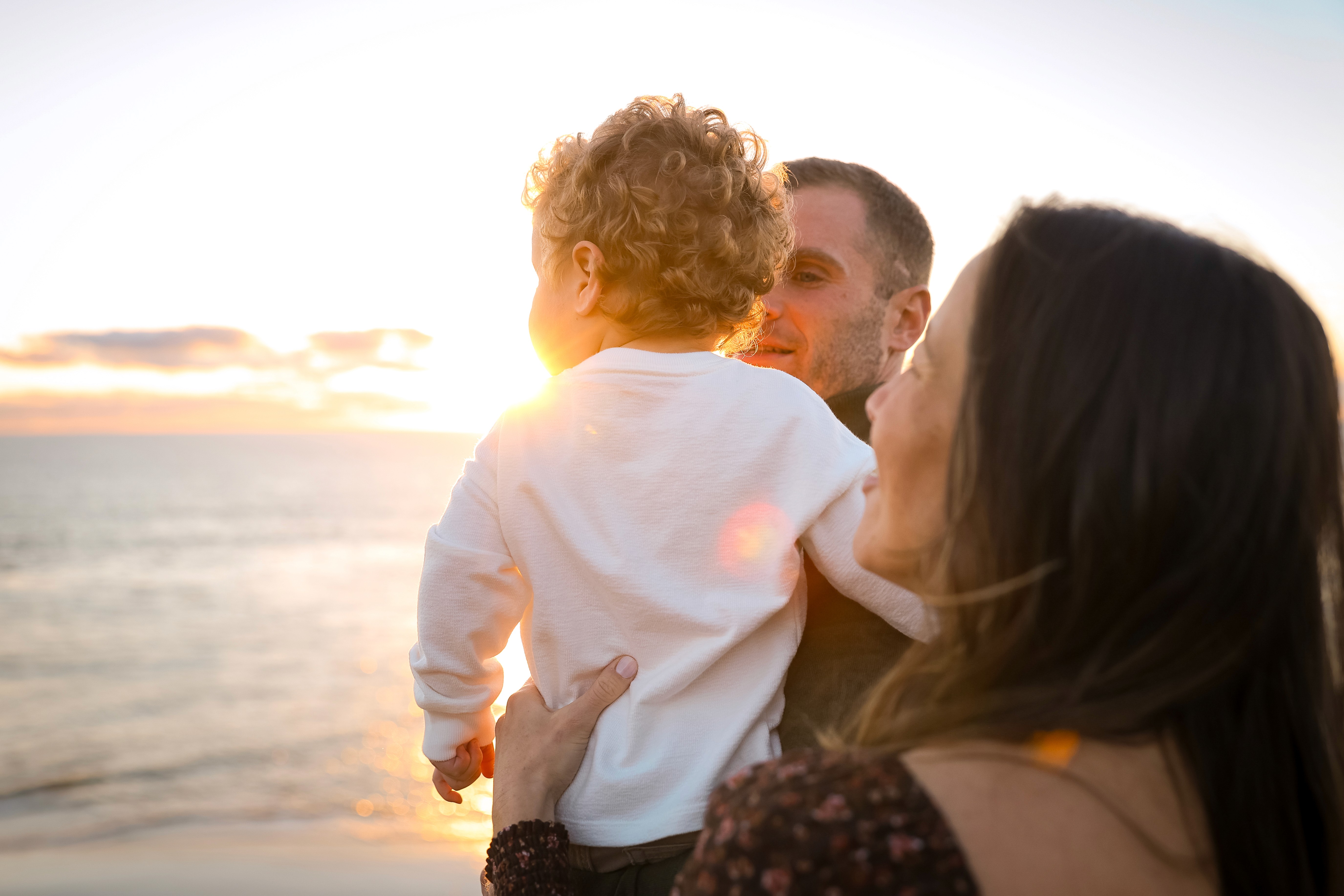 Family walking together by the ocean, during a sunset maternity shoot.