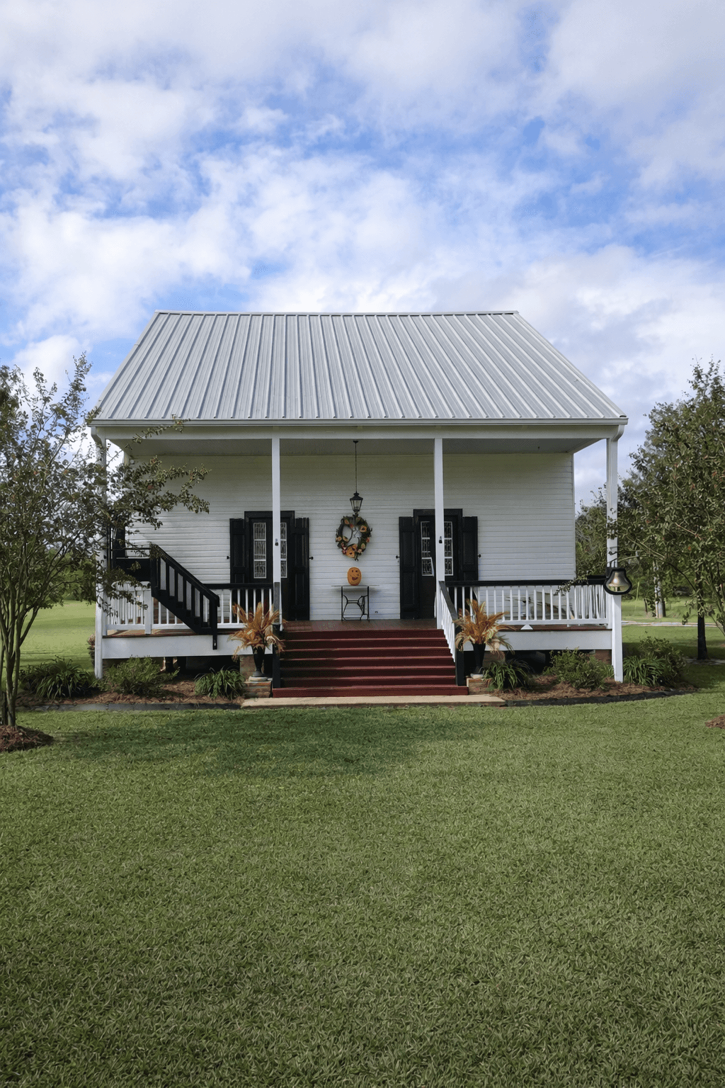 A modern, luxury beachfront villa with large glass windows and balconies overlooks a rocky shoreline, surrounded by palm trees at sunset.