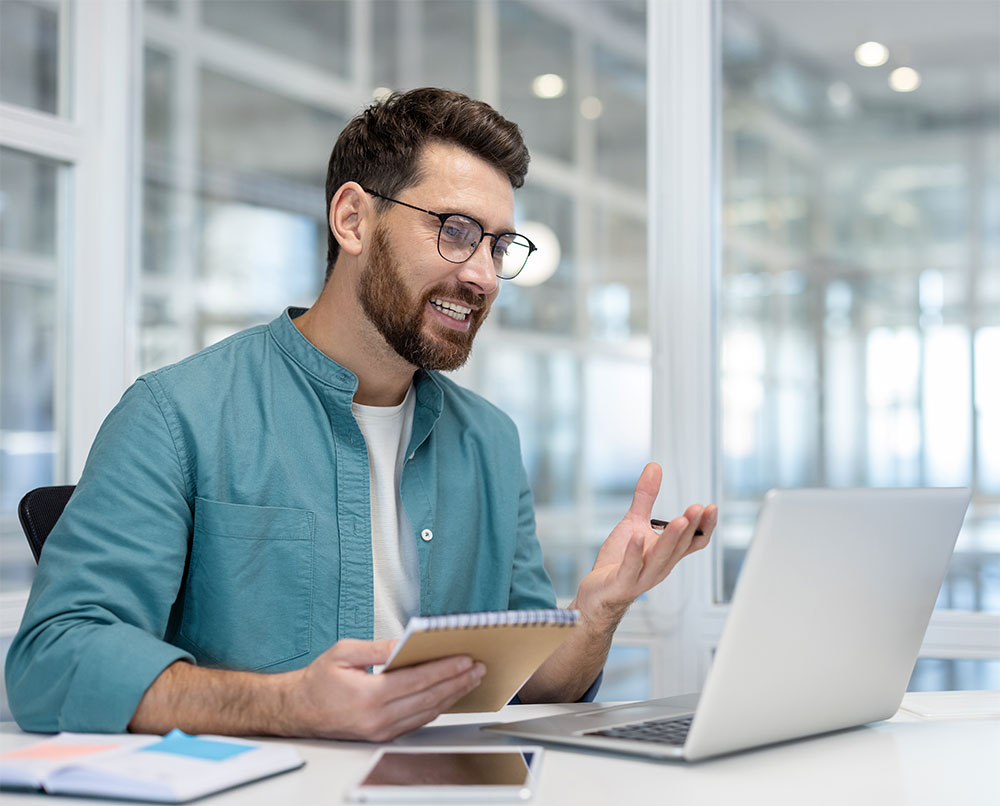 Ein Mann sitzt am Laptop und hält eine Videokonferenz ab.