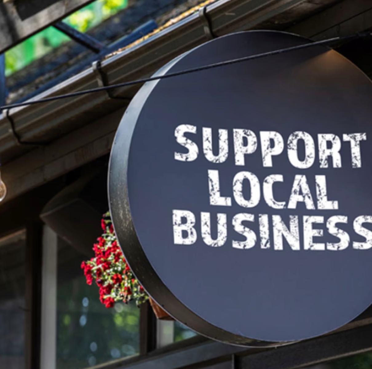 A smiling man with curly hair is sitting at a desk, looking at the camera, with a laptop and a lamp in the background.