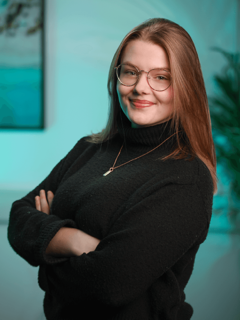 A woman with short curly hair wearing a black t-shirt looks into the camera.