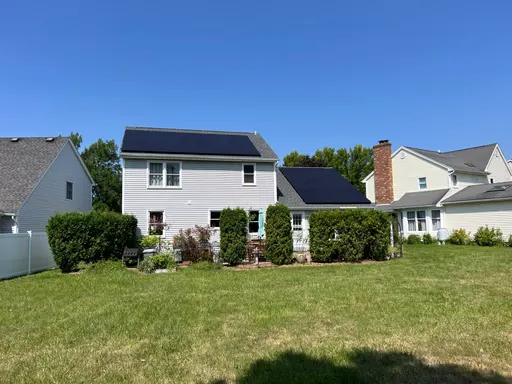 Residential rooftop solar panels installed on a white two-story home with a large backyard.