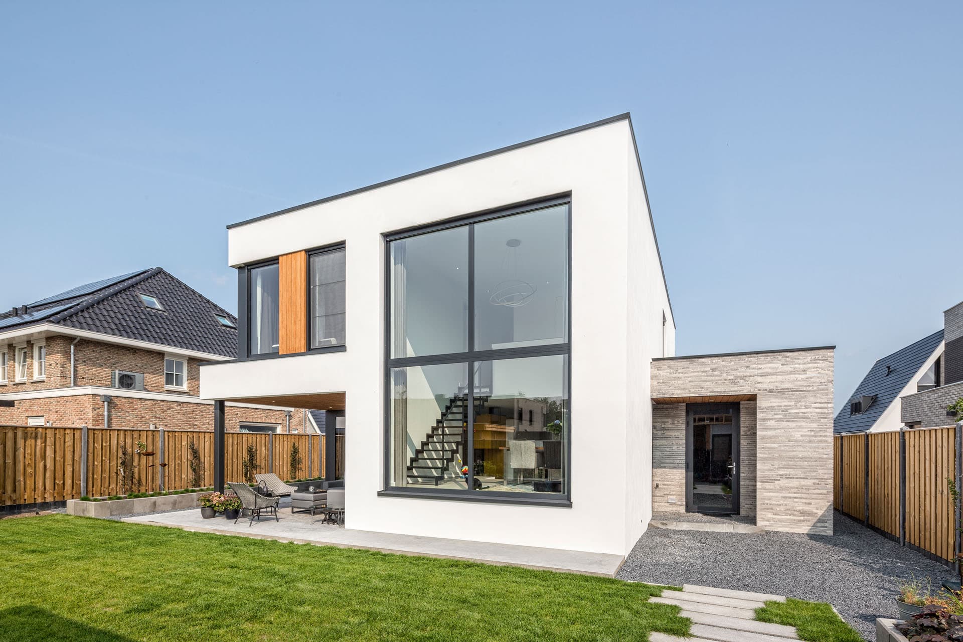Tuinzijde van moderne villa in Apeldoorn met groot raam, overdekt terras en vrijstaand bijgebouw
