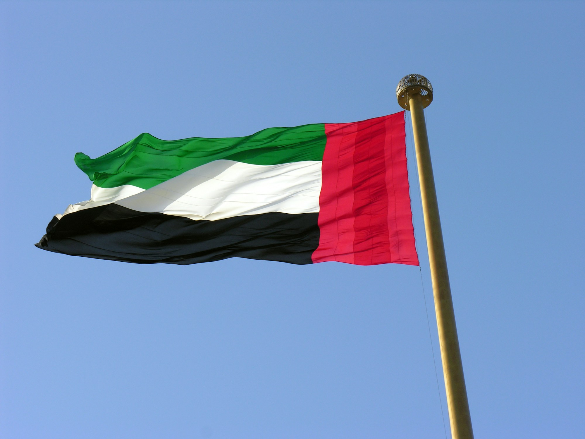 Large UAE flag waving on a flagpole against a clear blue sky
