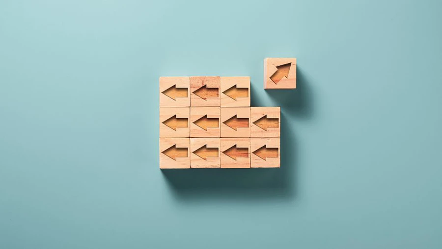 Wooden blocks with arrows pointing left, except one block pointing right, symbolizing innovation or thinking differently.
