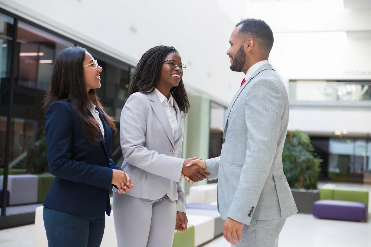 Two women in professional suits shaking hands with a businessman during a meeting for low-risk business ideas in Dubai.