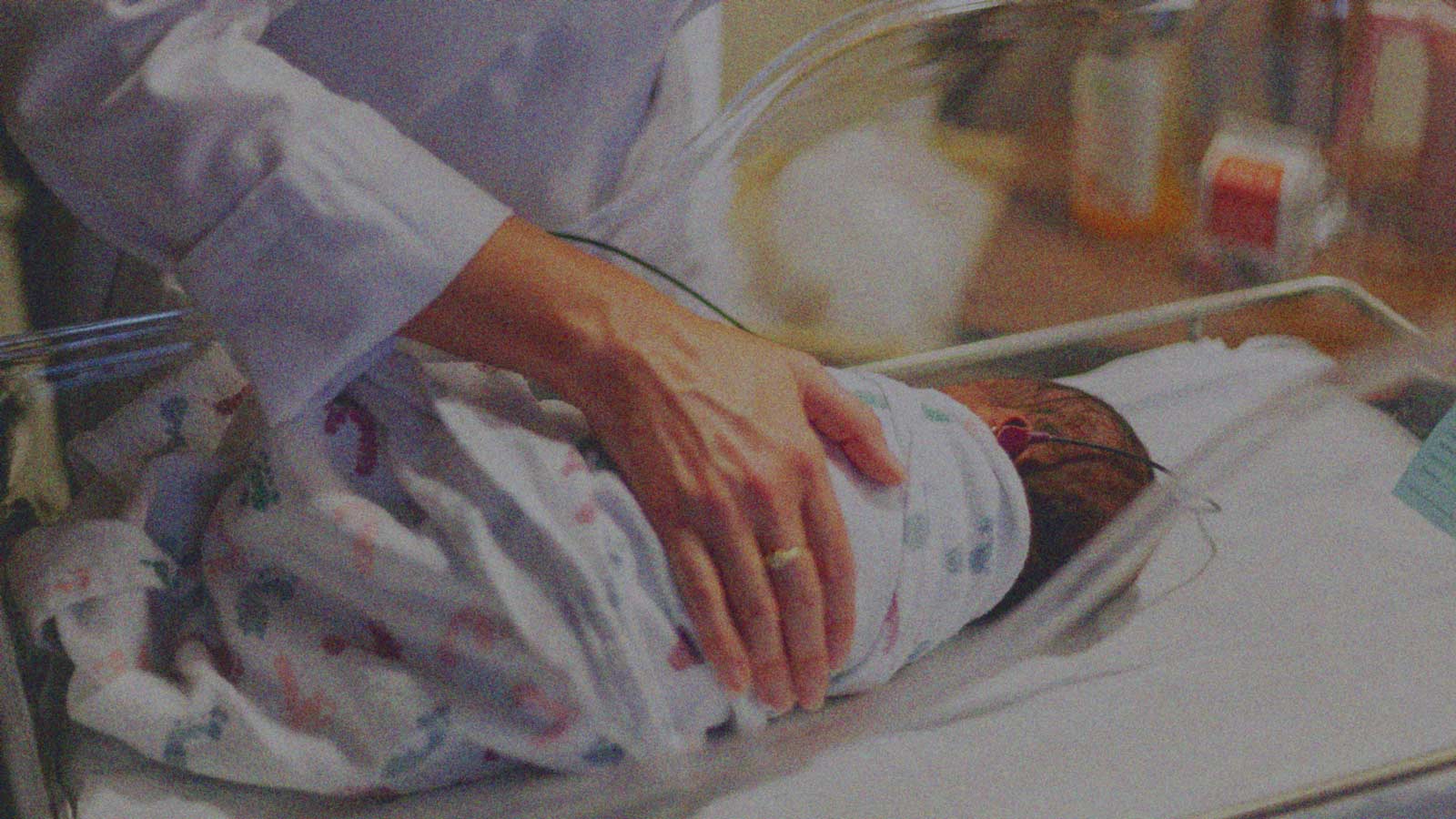 Foto que muestra la mano de una persona reposando sobre un bebé recién nacido en un hospital, en la columna de opinión Dignidad y «temas valóricos» de IdeaPaís.