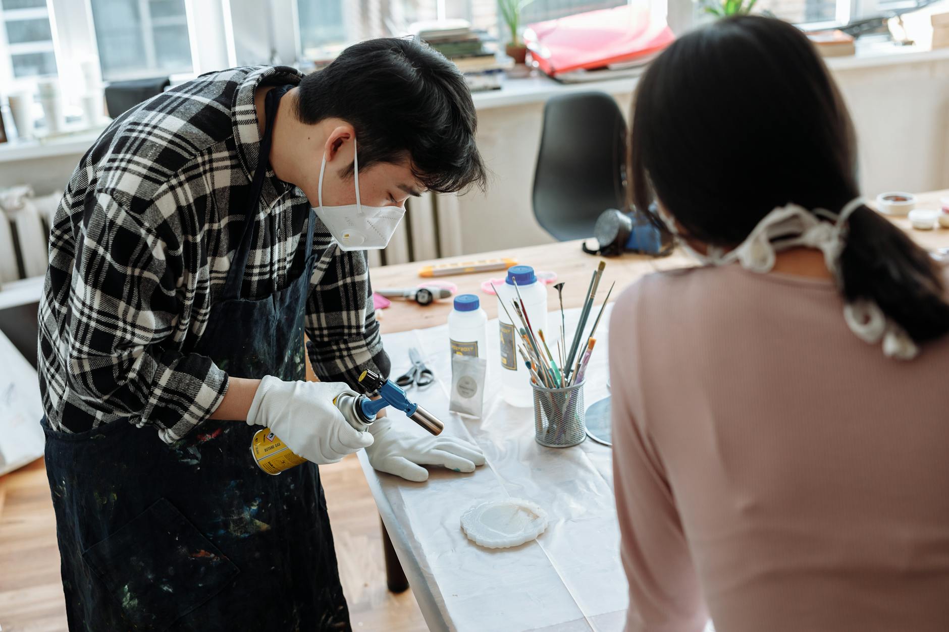 Two individuals collaborating on a resin art project inside a bright studio.