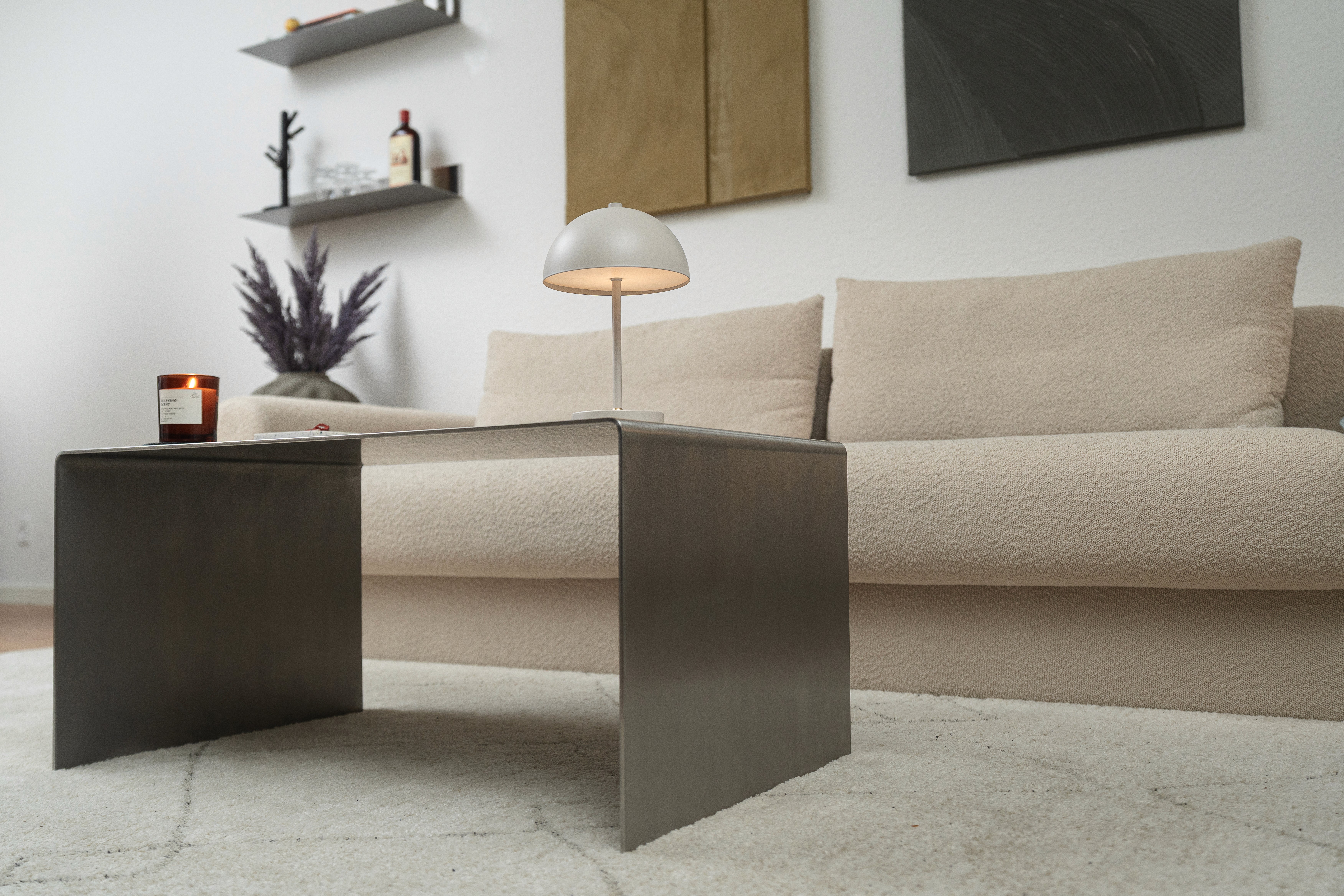 A person wearing a beige sweater and pants, with sunglasses, leans against a sunlit wall. The scene conveys a calm and relaxed atmosphere.