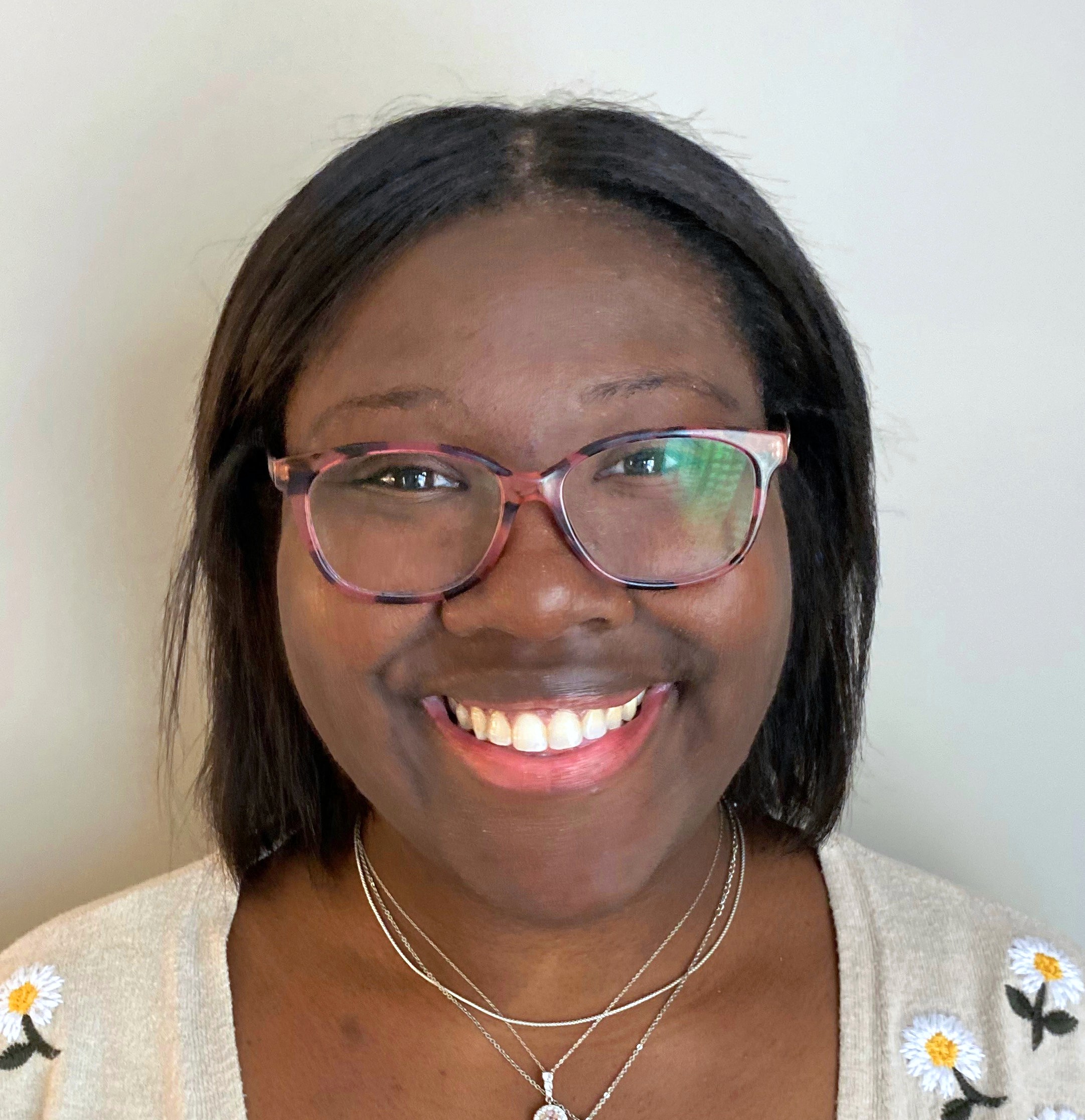 Smiling female therapist with short gray hair, wearing a brown top and a purple shawl, surrounded by a cozy background.