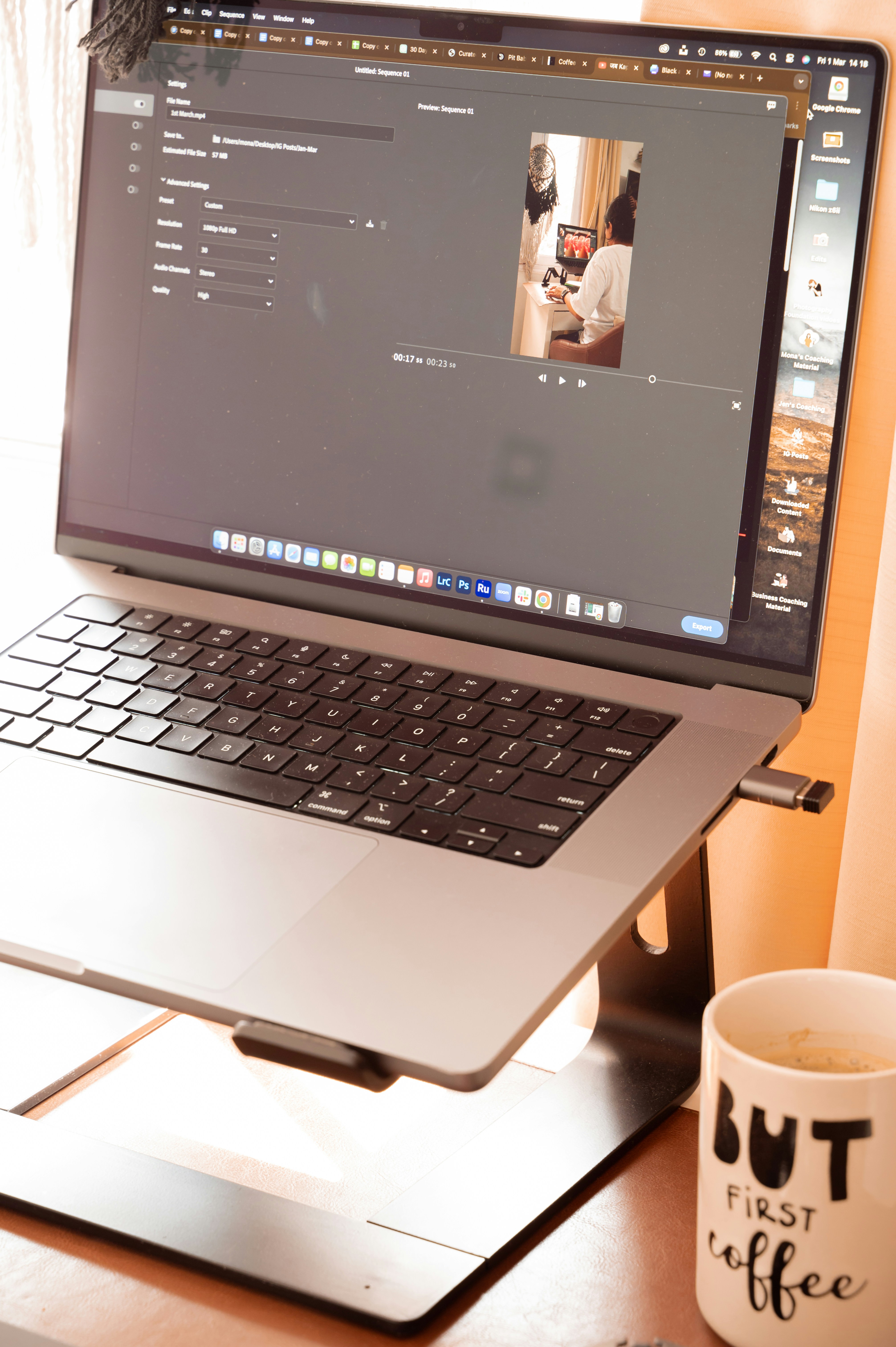 A sleek laptop on a stand displays a photo editing software interface, while a white mug with the text "But First Coffee" sits beside it on a wooden desk, suggesting a cozy and productive workspace.