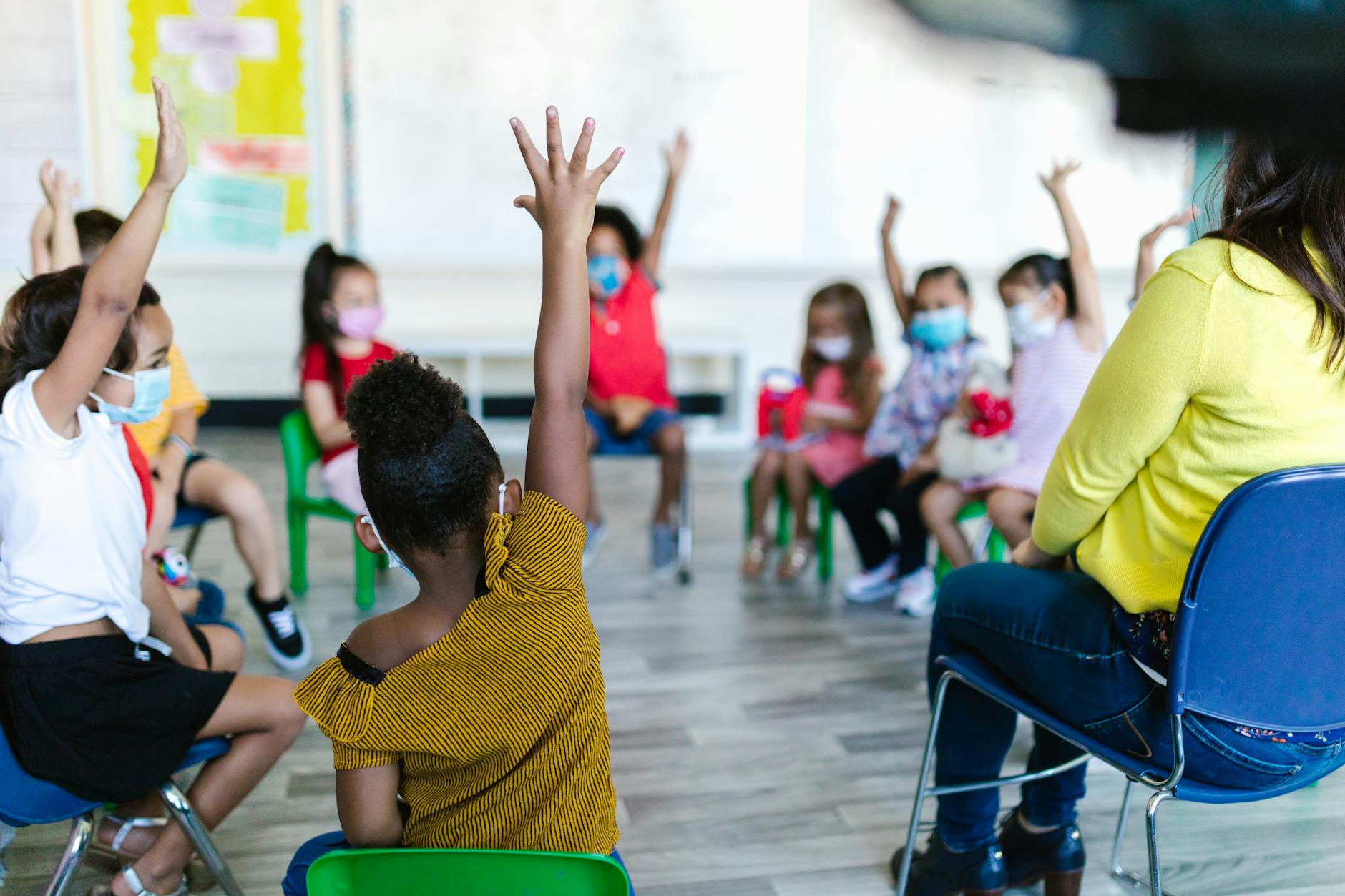 Diverse elementary students raising their hands and smiling during a lesson with interactive teaching tools.