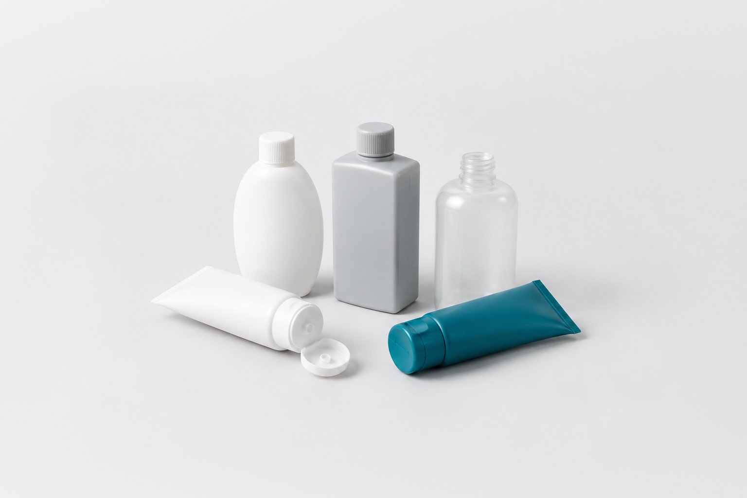 Unlabelled blow-moulded bottles in white, grey and clear plastic with two squeeze tubes, one tube in teal