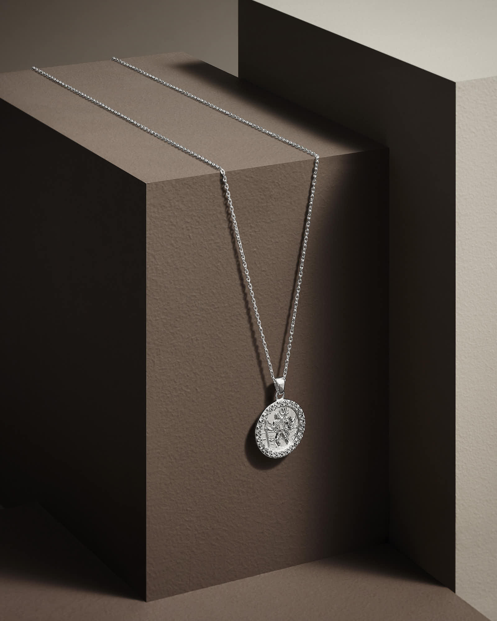 A pendant necklace hangs against geometric brown backgrounds, highlighting its design and elegance.