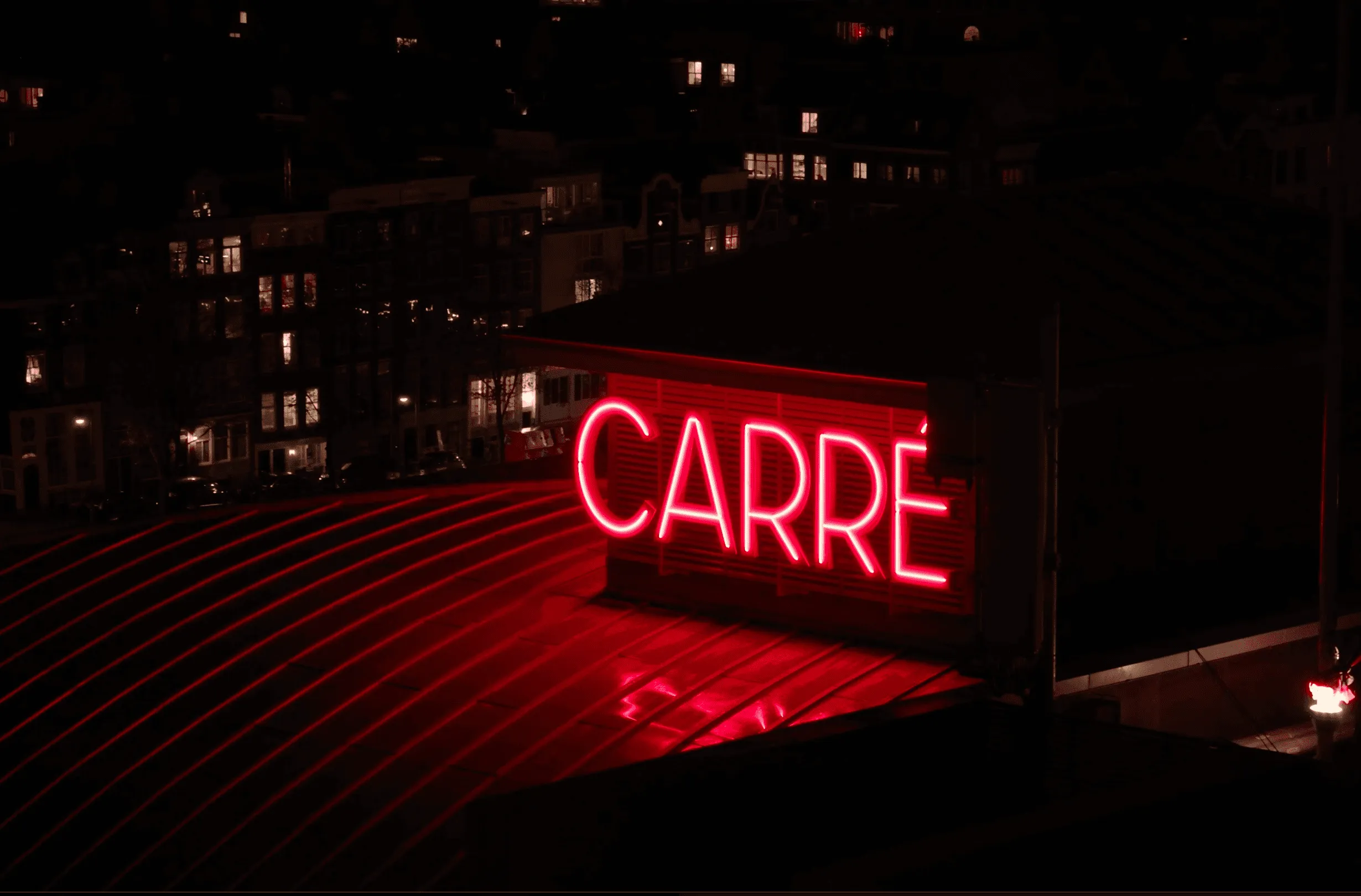 A glowing red sign displaying the word "CADRE" against a dark background, with faint lights in the distance.