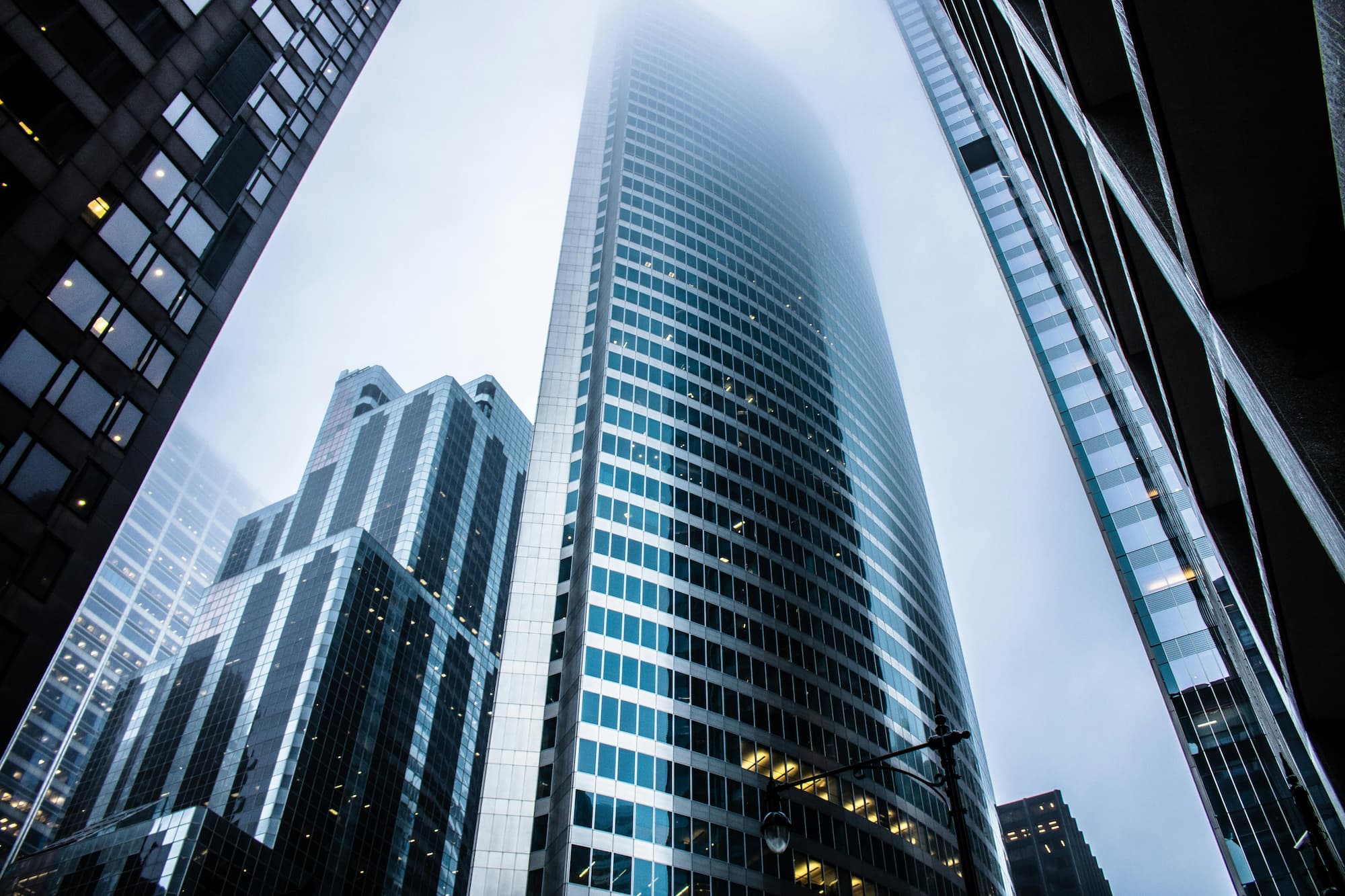 Low-angle view of towering glass skyscrapers reaching into the fog