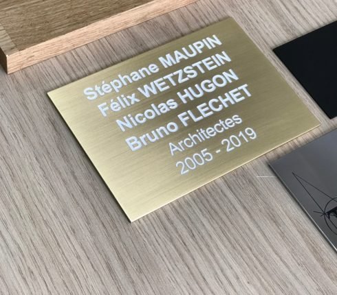 Gravure mecanique fabriqué par LeGraveur sur une surface en bois avec inscription gravée en blanc indiquant les noms et les dates : Stéphane Maupin, Félix Wetzstein, Nicolas Hugon, Bruno Flechet, Architectes, 2005-2019.