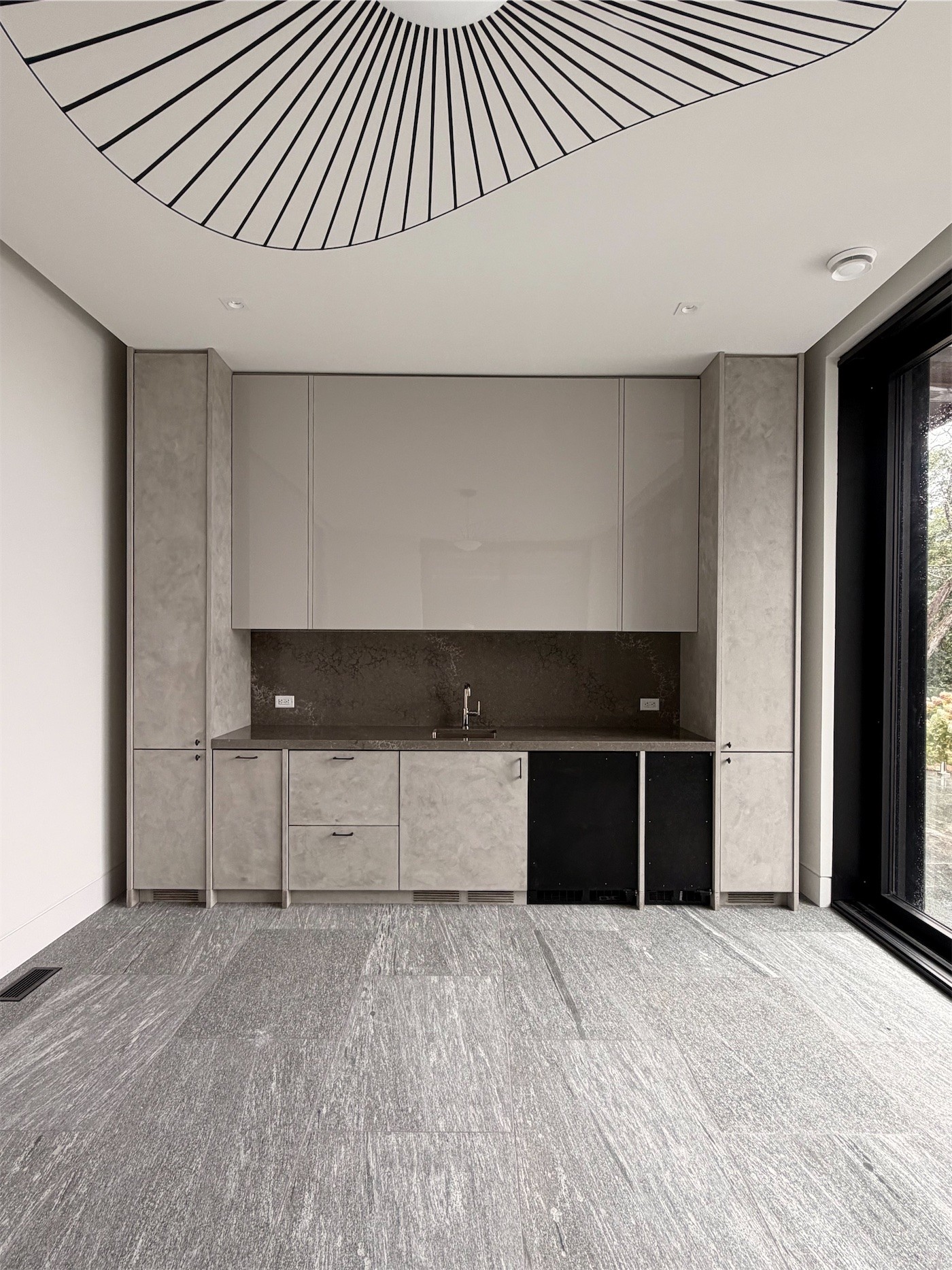 A kitchenette in pale stone and dark wood under a sculptural pendant