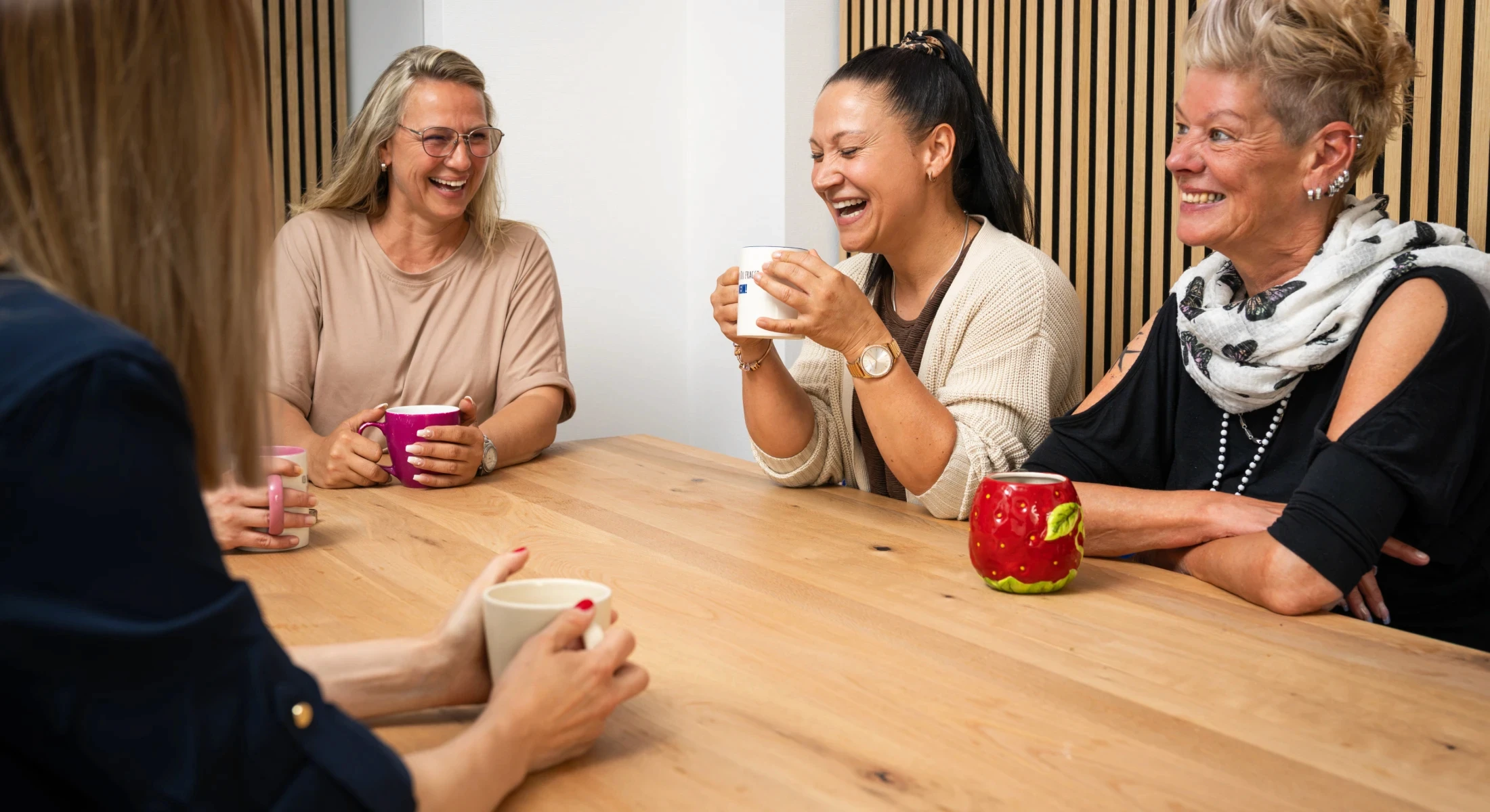 GJP-Mitarbeiterinnen sitzen lachend zusammen an einem Holztisch