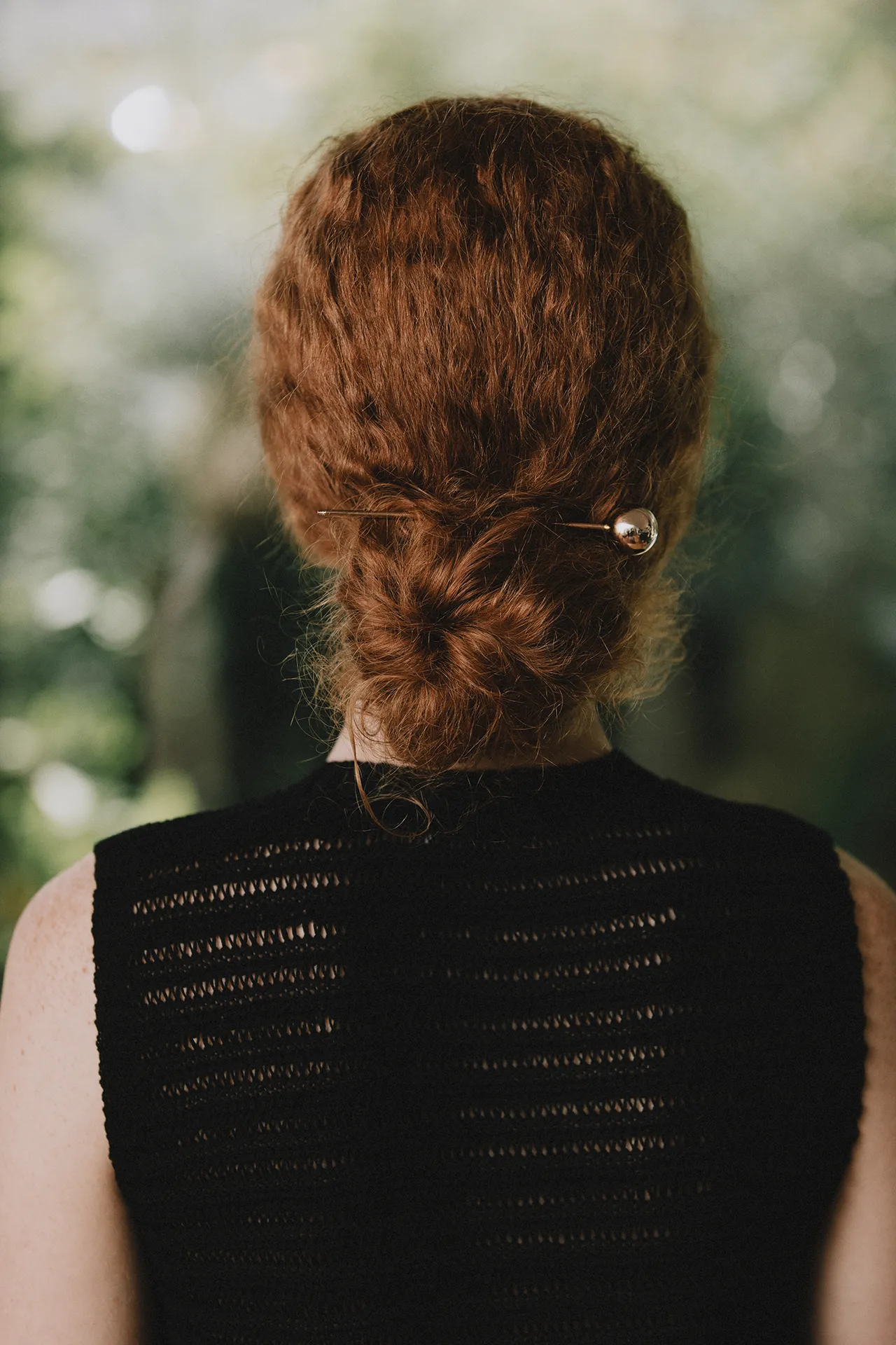 Rear view of a model wearing an Annapurna SS26 black open-knit top with red hair styled in a bun.