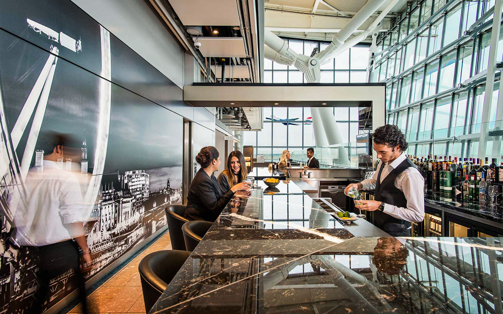 Heathrow Plaza Premium Lounge bar with bartender serving drinks and guests seated at the counter.